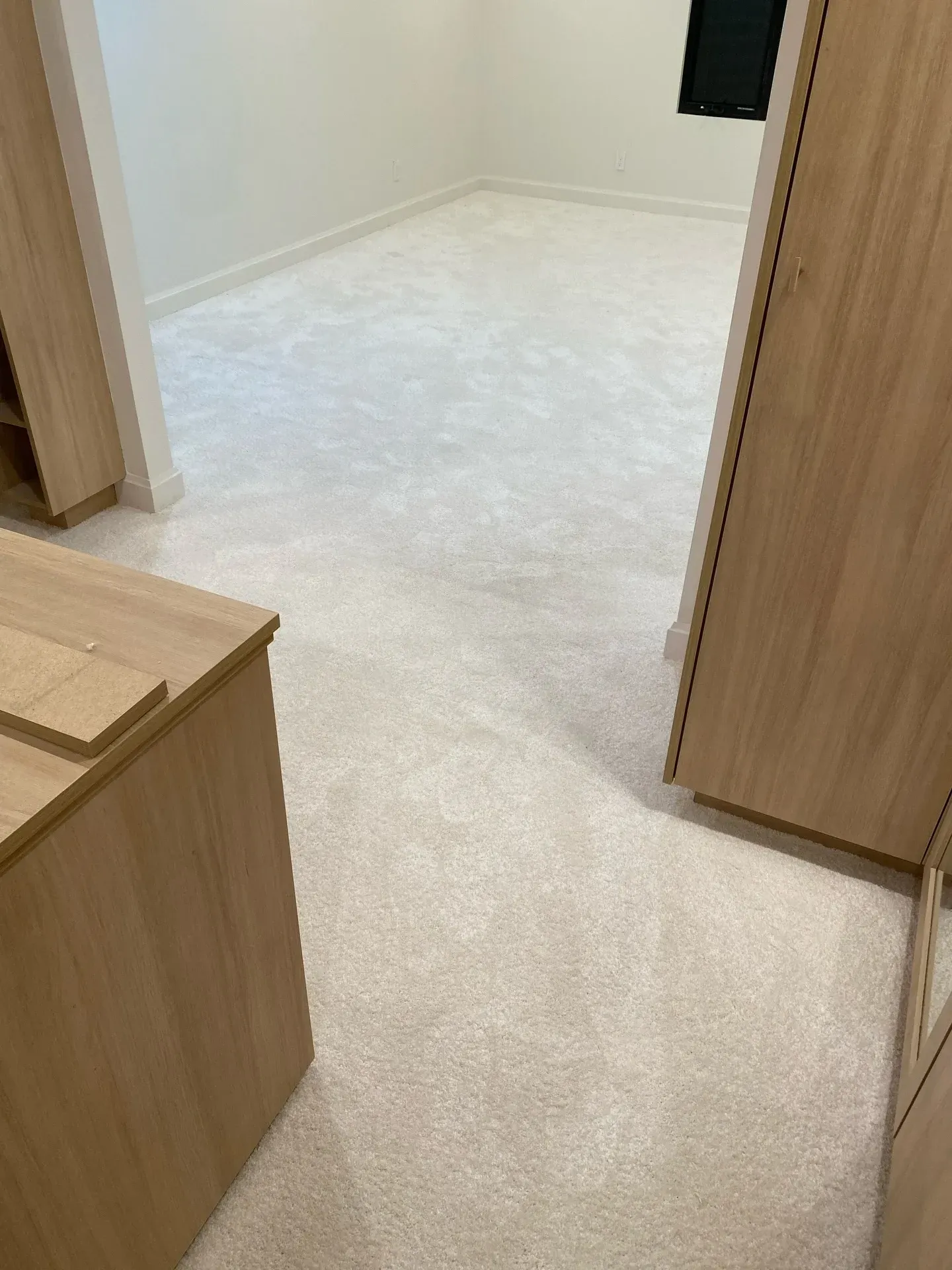 Narrow carpeted hallway with light wood cabinets and a doorway into a white room