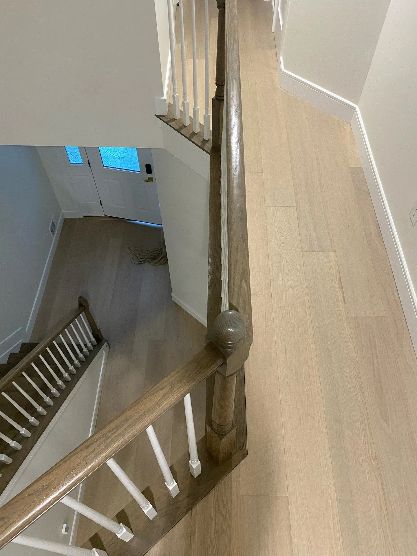 Staircase landing with wood railings and beige walls, looking down to a lower hallway with windows.