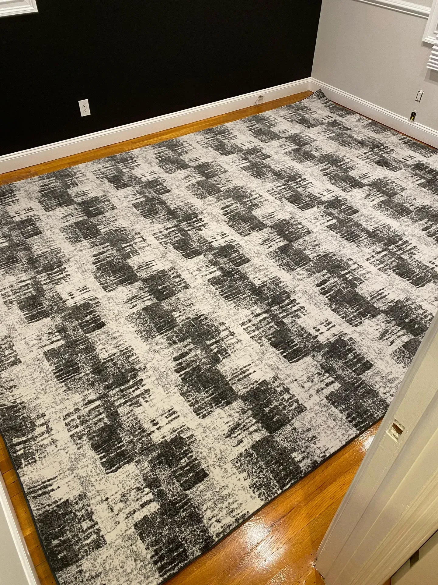 Empty room with gray patterned rug, black accent wall, and hardwood floor trim