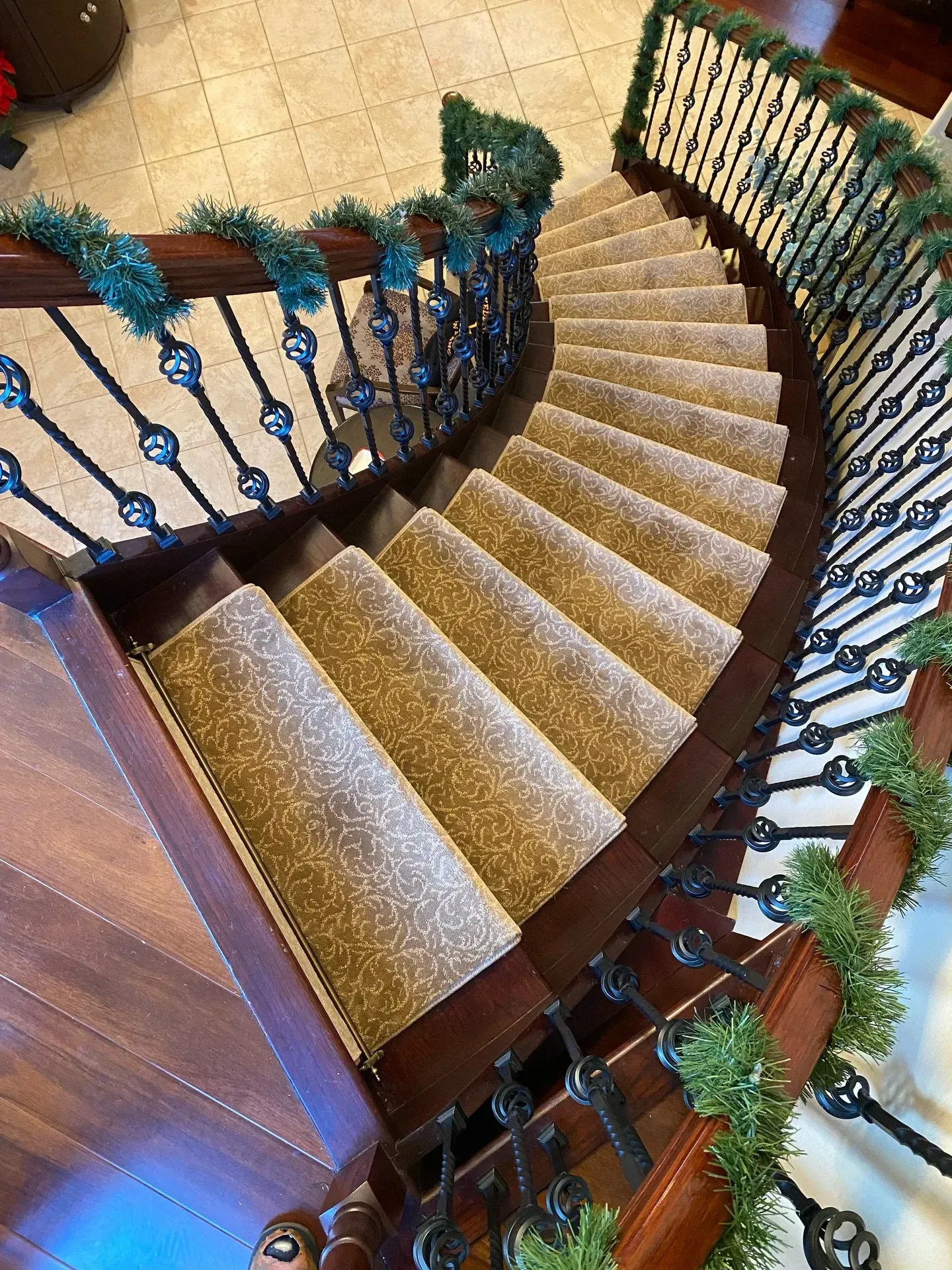 Curved carpeted staircase with black wrought-iron railings and green garlands in a wood-floored interior