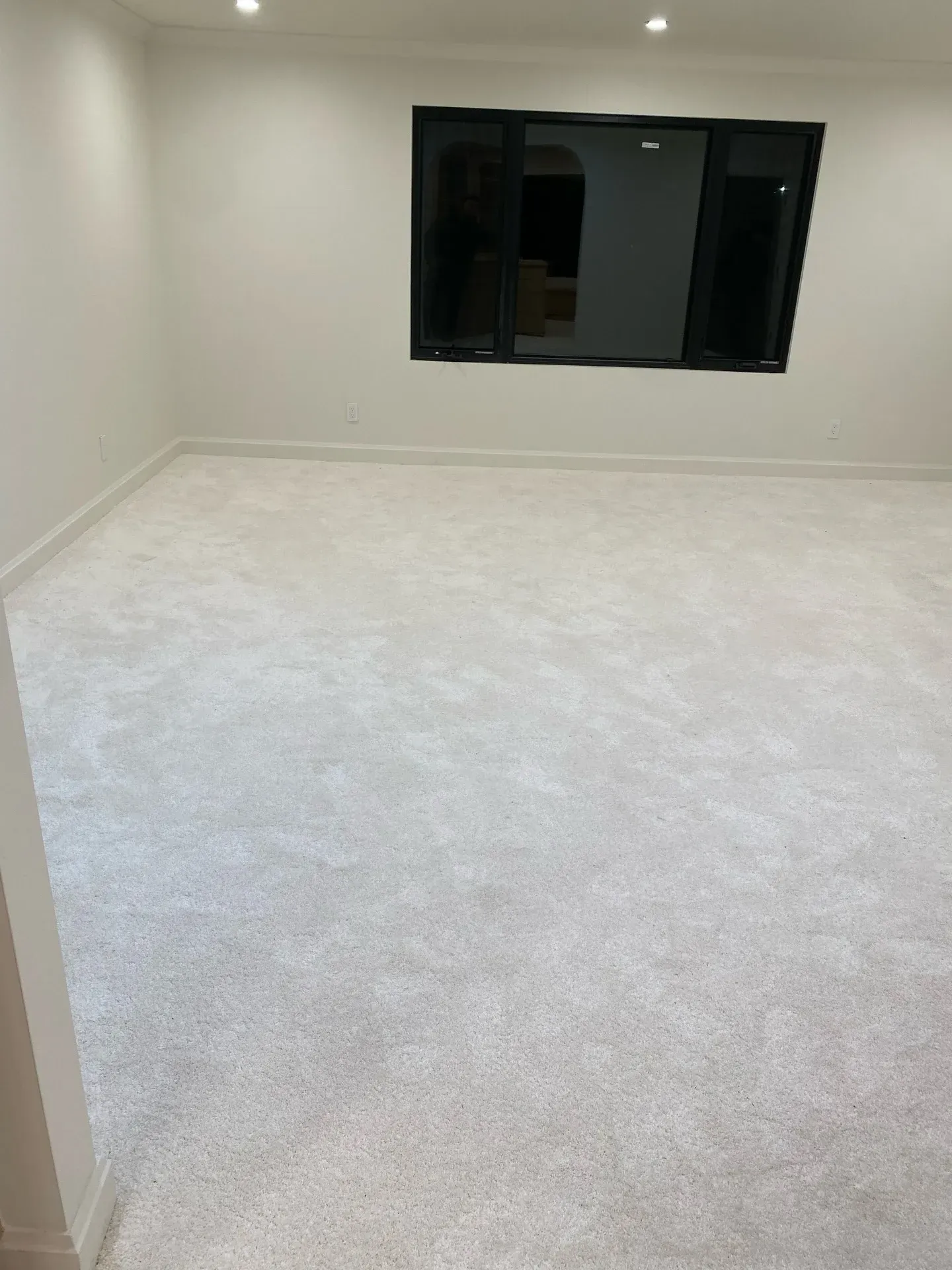 Empty carpeted room with white walls and a dark window on the far wall.