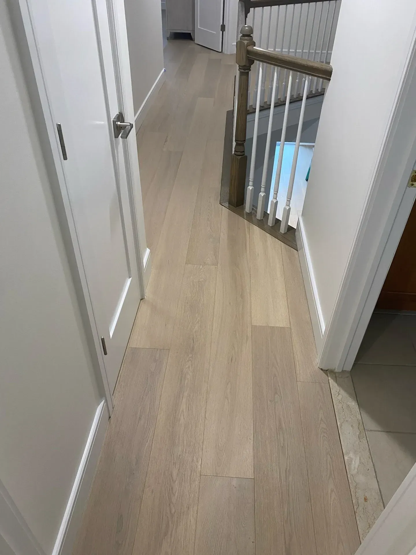 Narrow upstairs hallway with light wood flooring, white walls, and a baby gate at the end near stairs