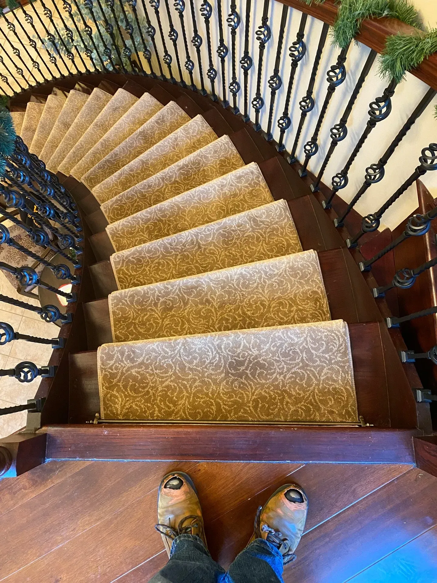 View down a curved carpeted staircase with ornate black railings, seen from the top.