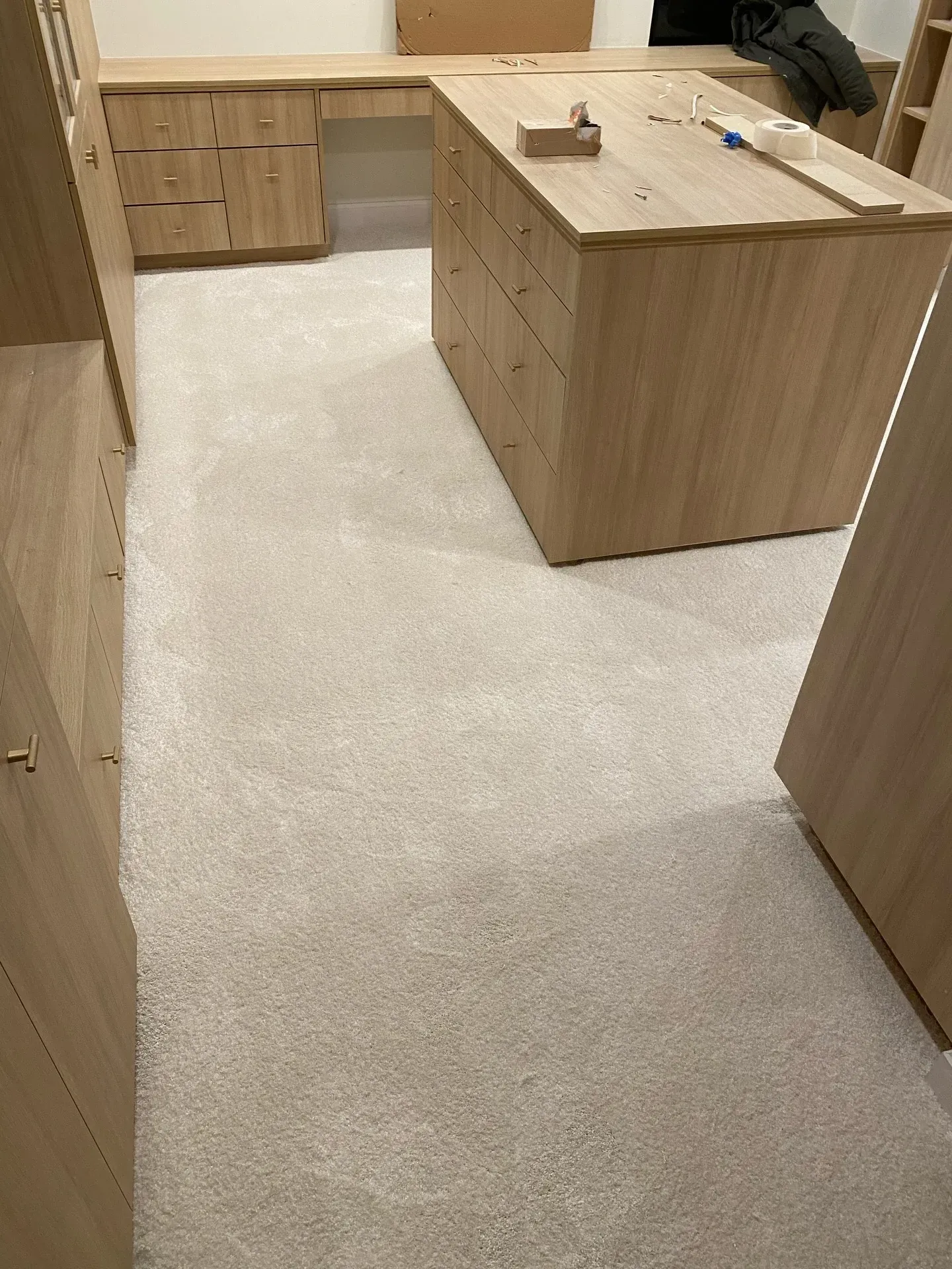 Empty modern kitchen with wood cabinets, light countertop, and carpeted floor in the foreground