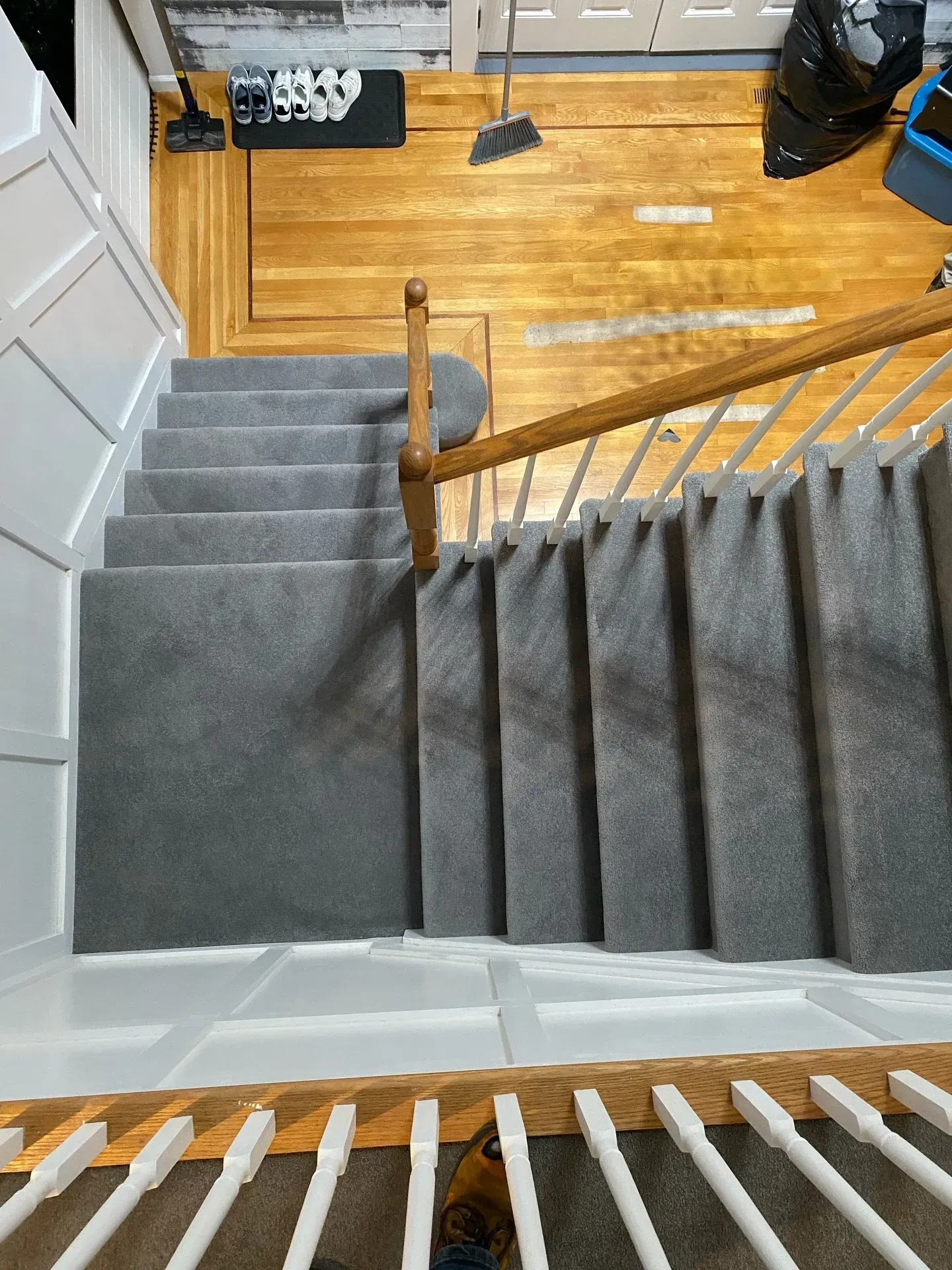Top-down view of carpeted stairs with wooden banister leading to a hardwood floor foyer.