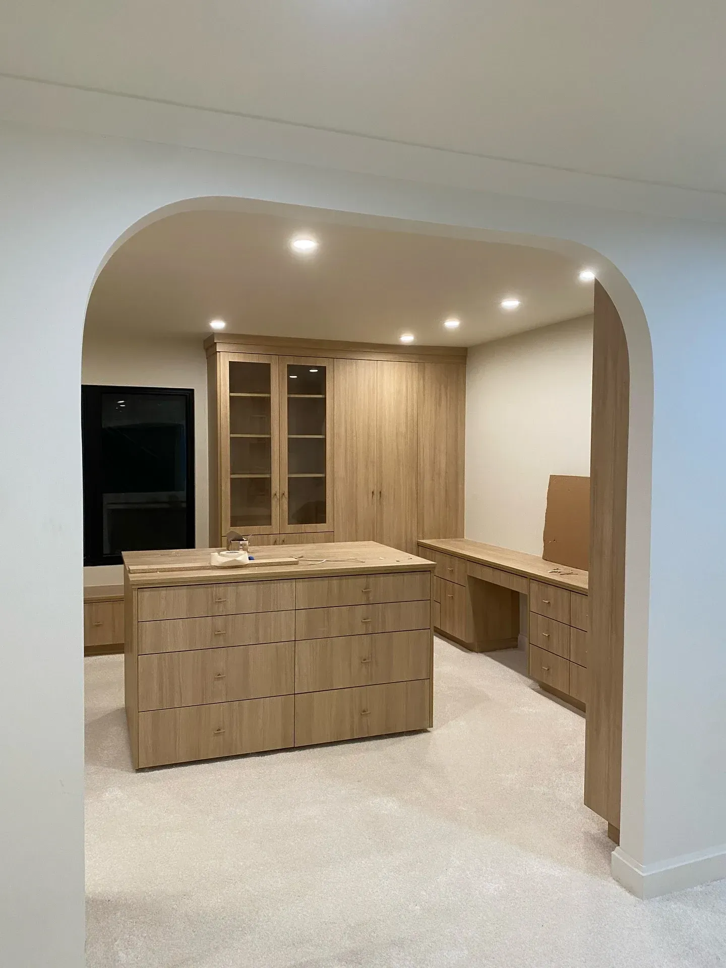 Modern kitchen with light wood cabinets, central island, and arched entryway.