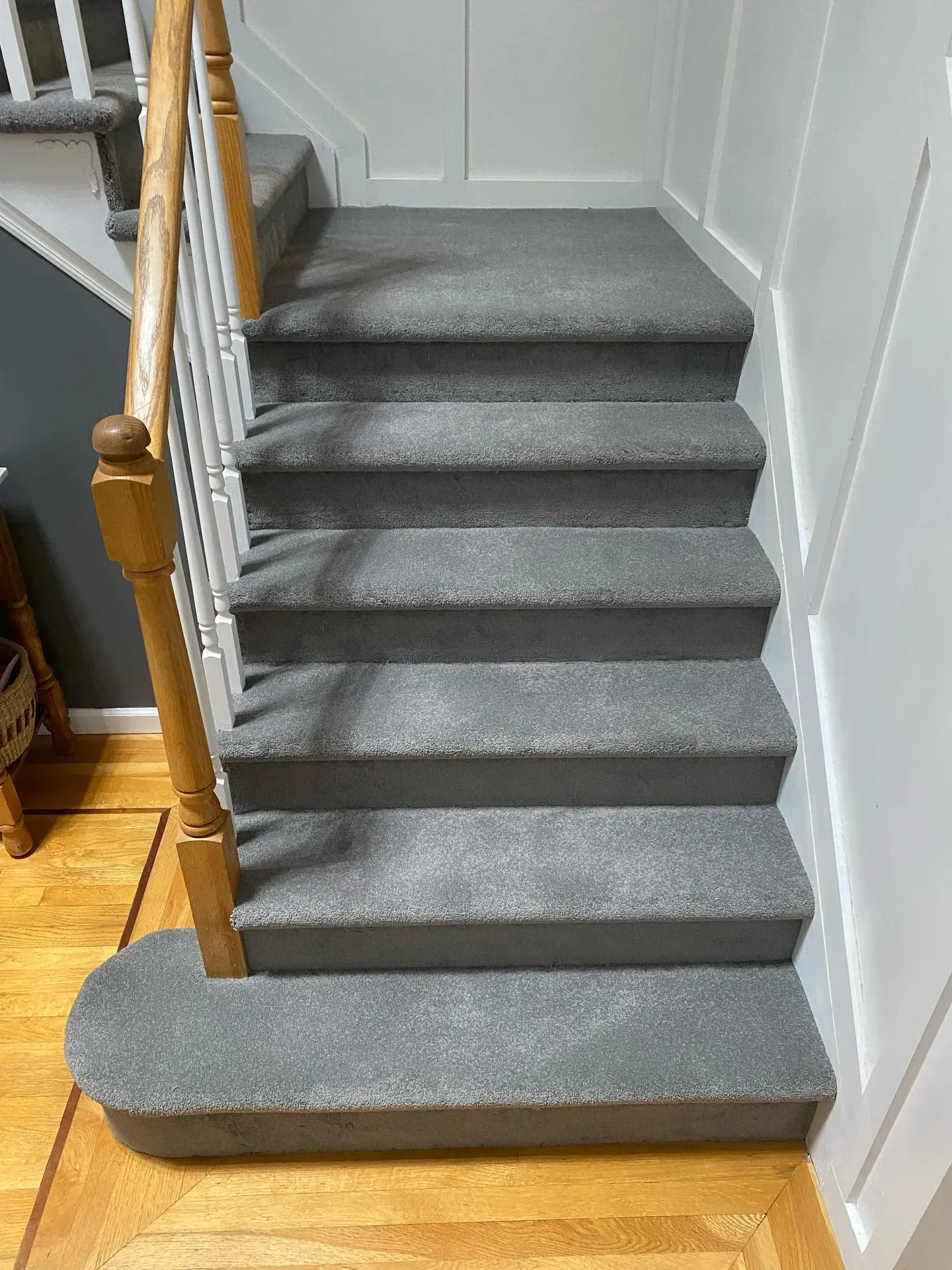 Carpeted indoor staircase with gray steps, white walls, and wooden handrails.