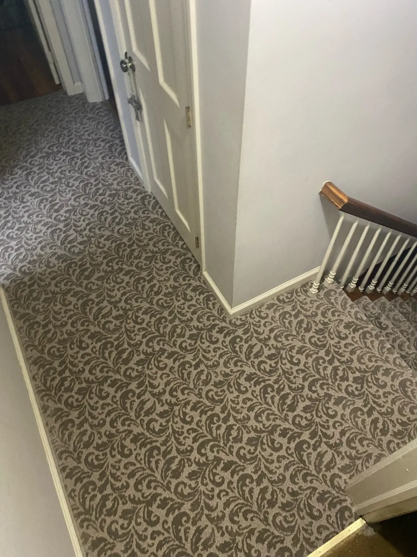 Carpeted hallway and staircase landing with white doors and beige walls.