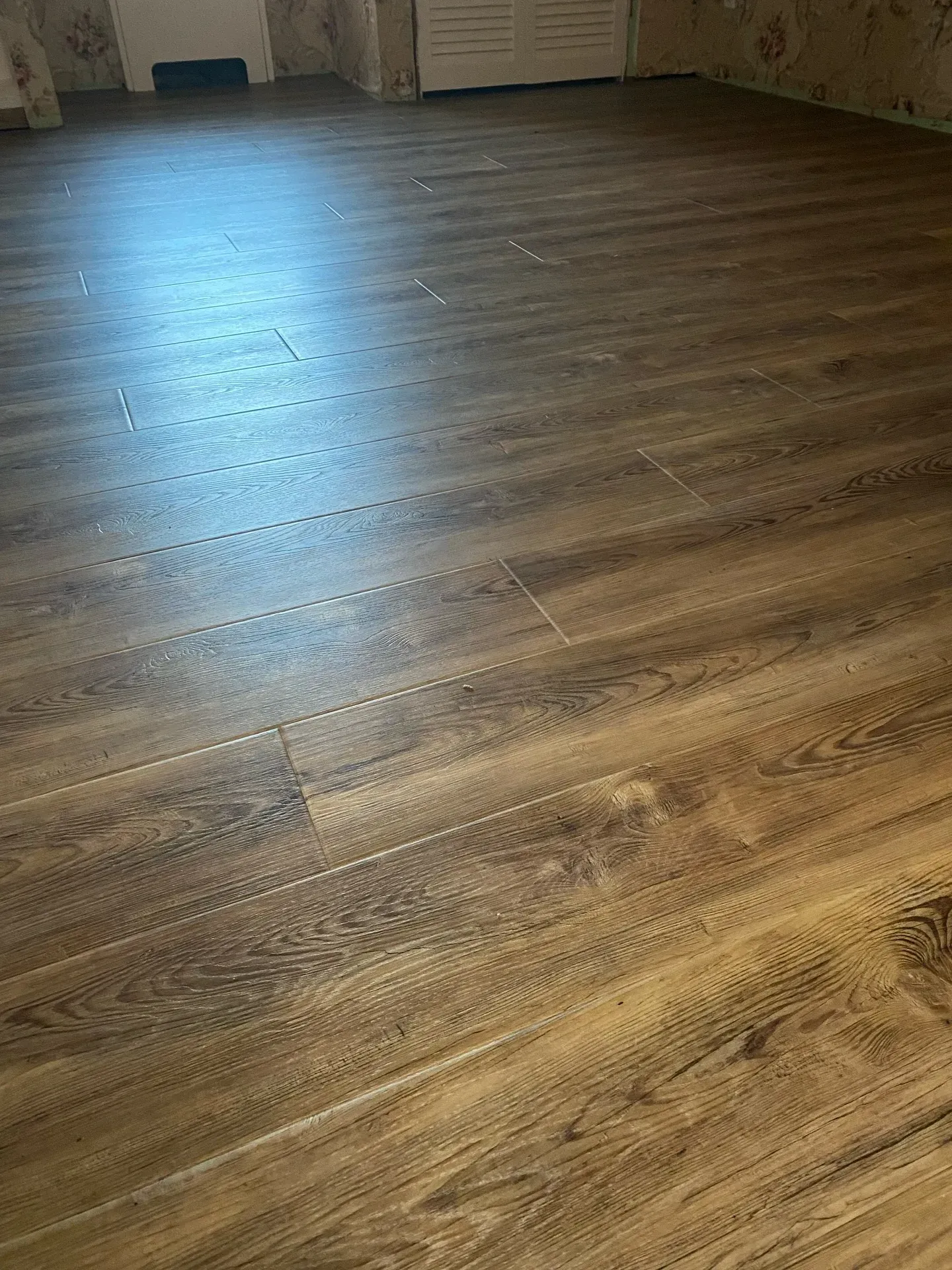 Wood-patterned laminate floor in a room with sunlight reflecting across it.