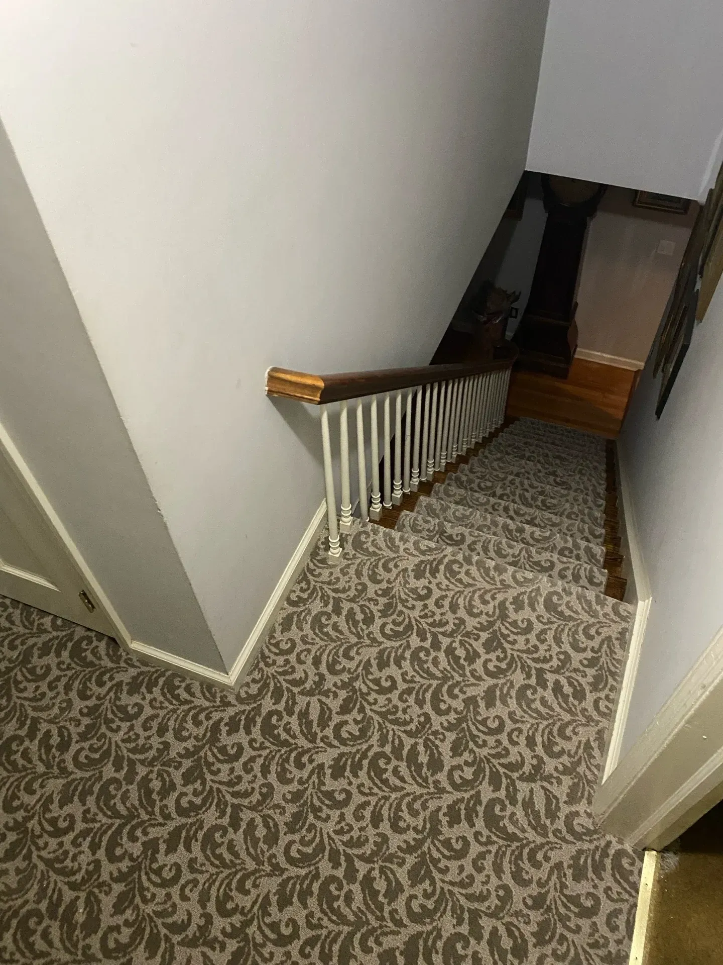 Carpeted staircase with white walls and wooden railing descending into a dim hallway.