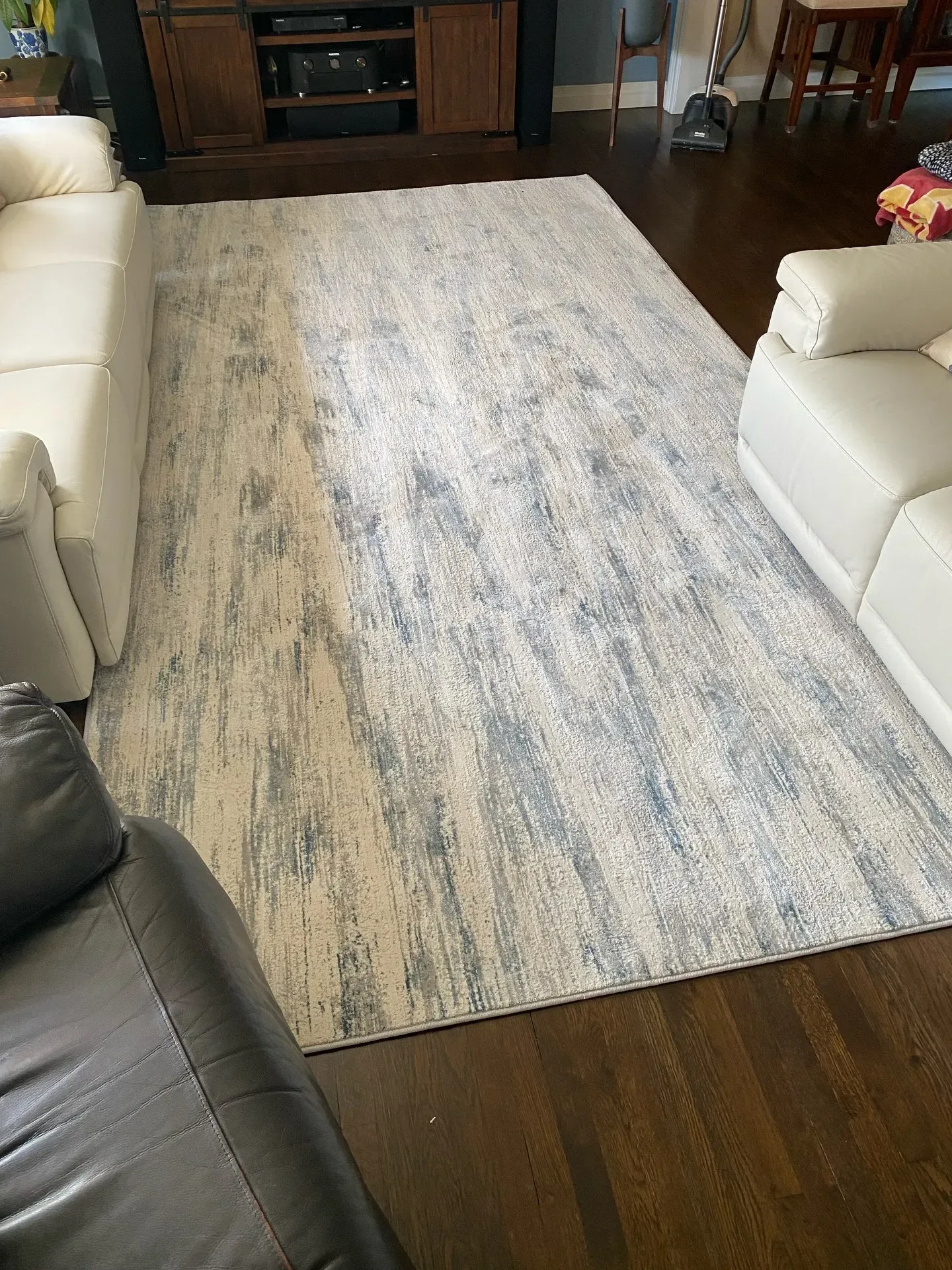 Light gray patterned area rug between white sofas on a dark wood floor in a living room