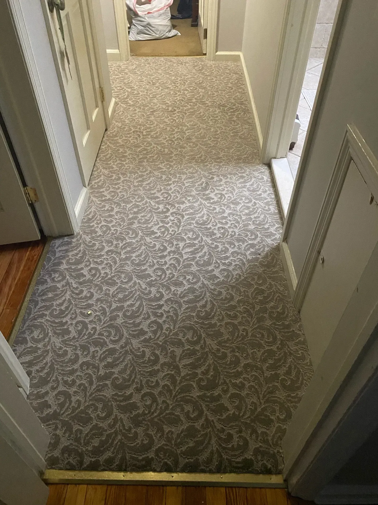 Narrow carpeted hallway with beige walls and a person partially visible at the far end.