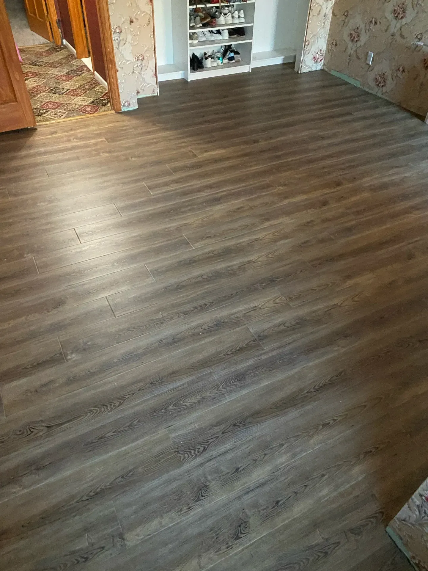 Empty room with gray-brown wood-look flooring and a small white shelf in the back.
