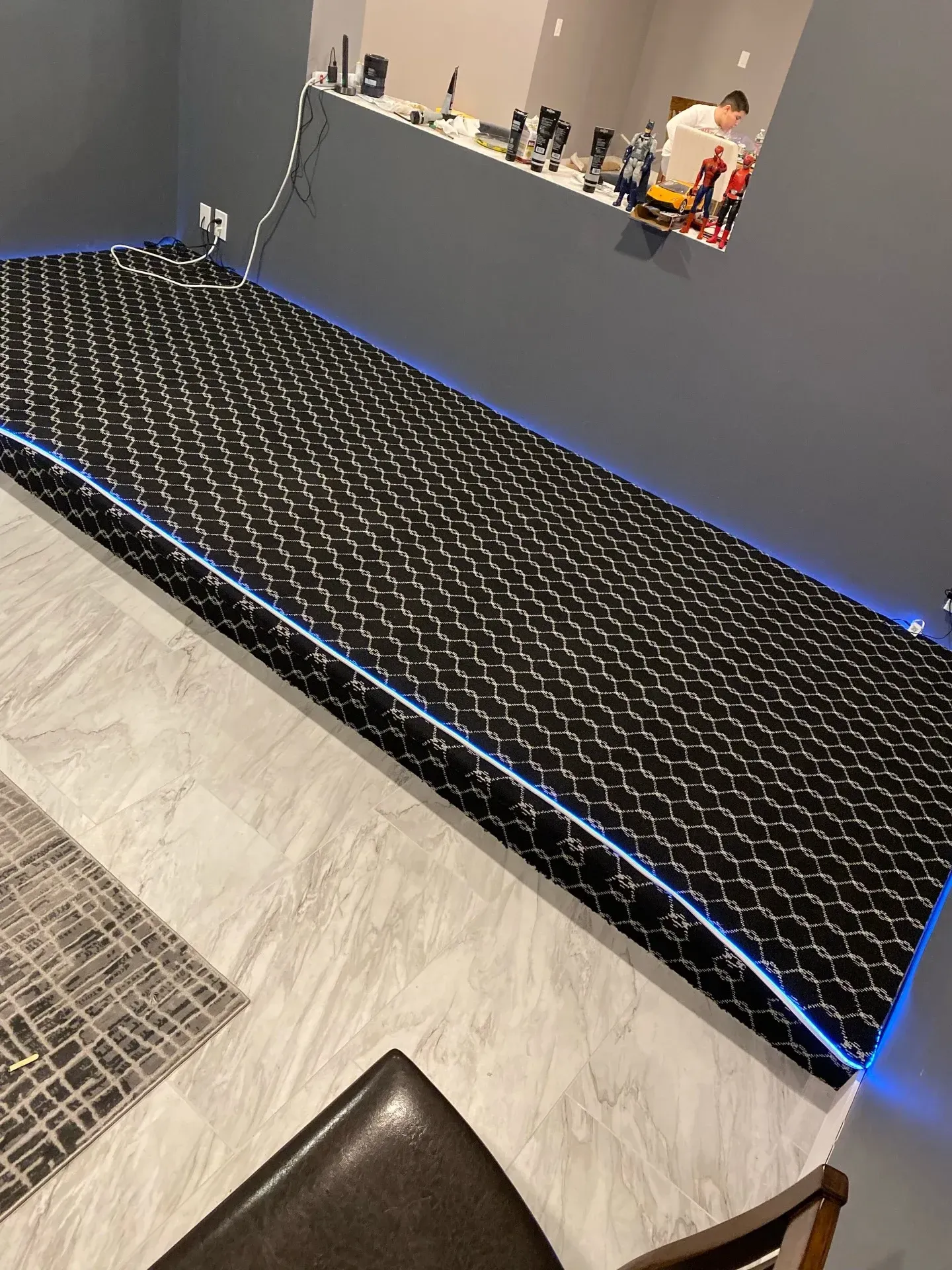 Fitness room with black cushioned mat floor and blue LED edge lighting along a gray wall.