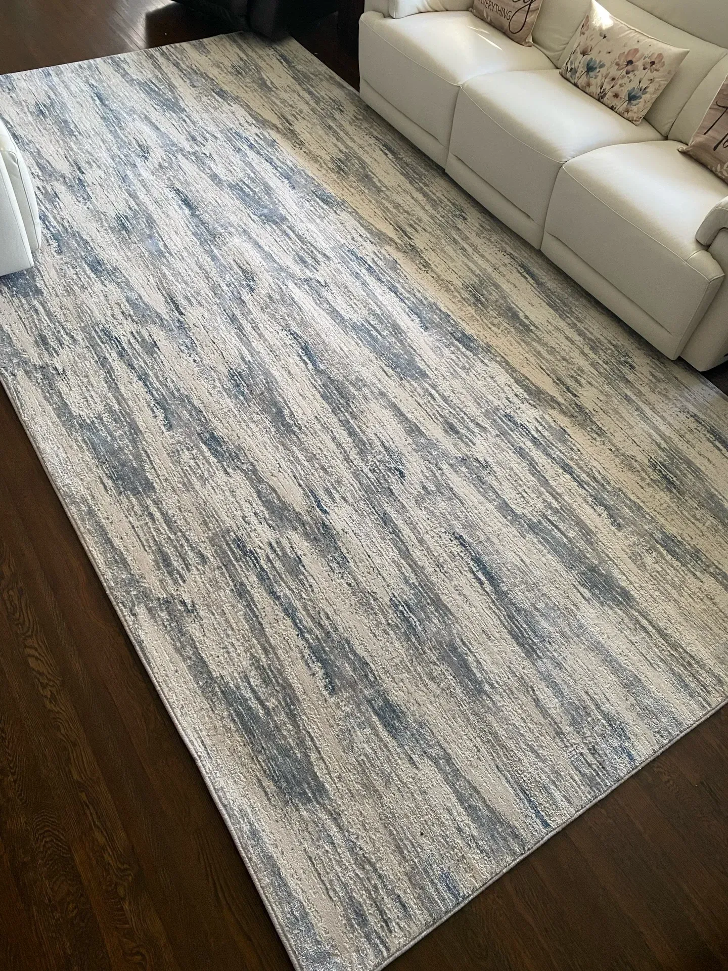 Light gray and blue patterned area rug beside a cream sofa on a dark wood floor.
