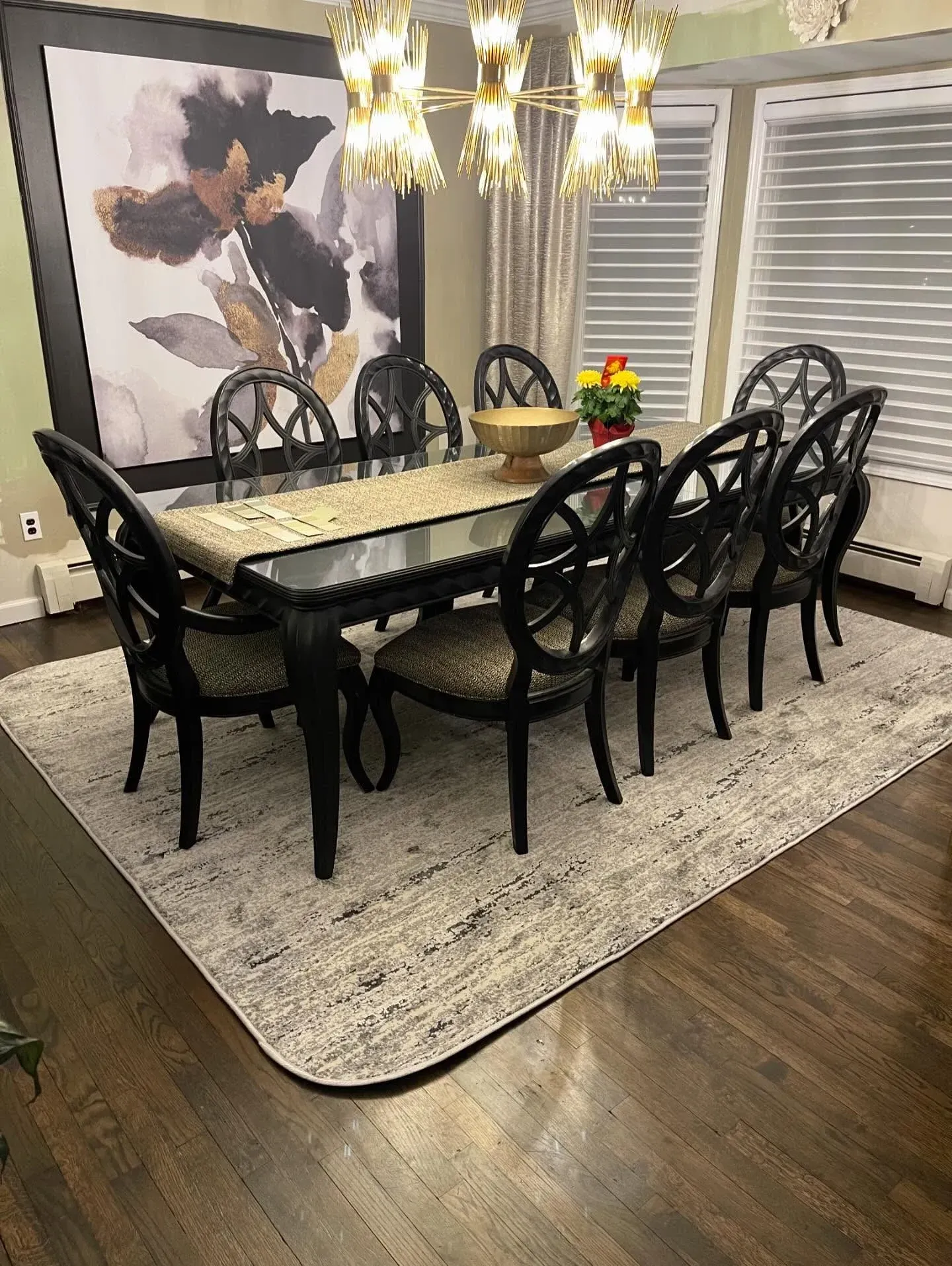Dining room with black chairs, a light table, chandelier, floral wall art, and a dark wood floor on a rug.