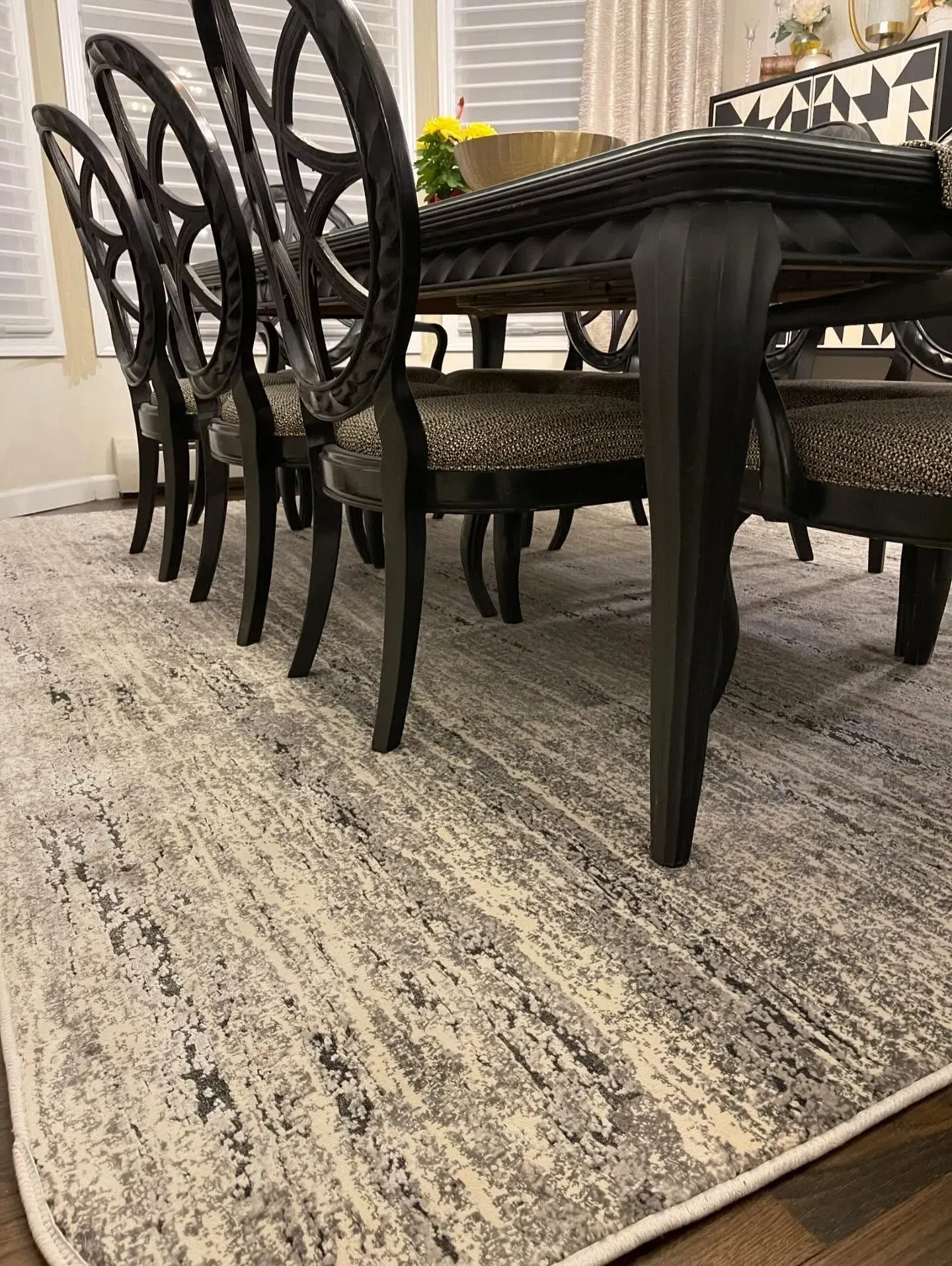 Black dining table with matching chairs on a light patterned rug in a bright room