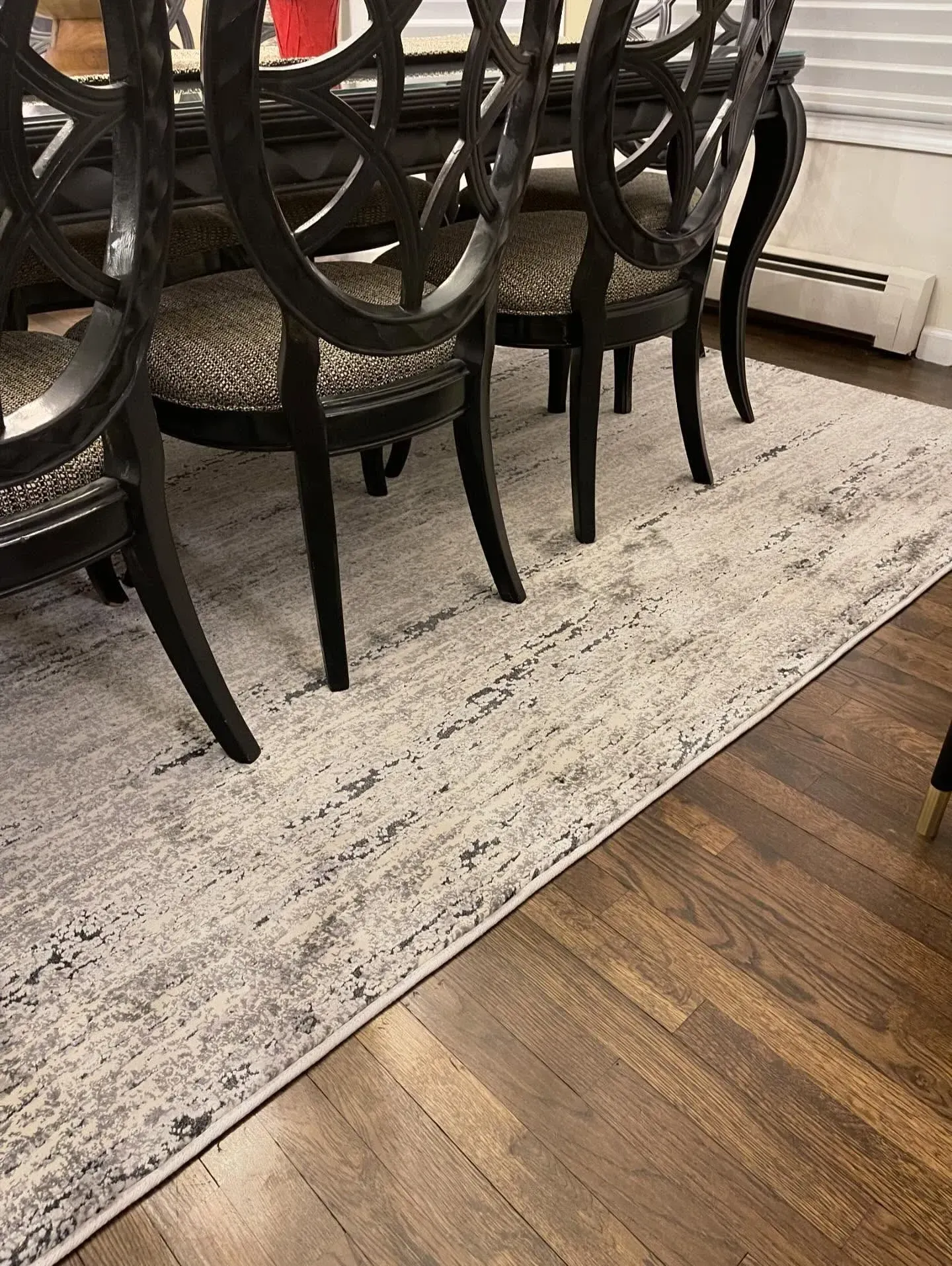 Black dining chairs around a table on a light patterned rug over hardwood floor.
