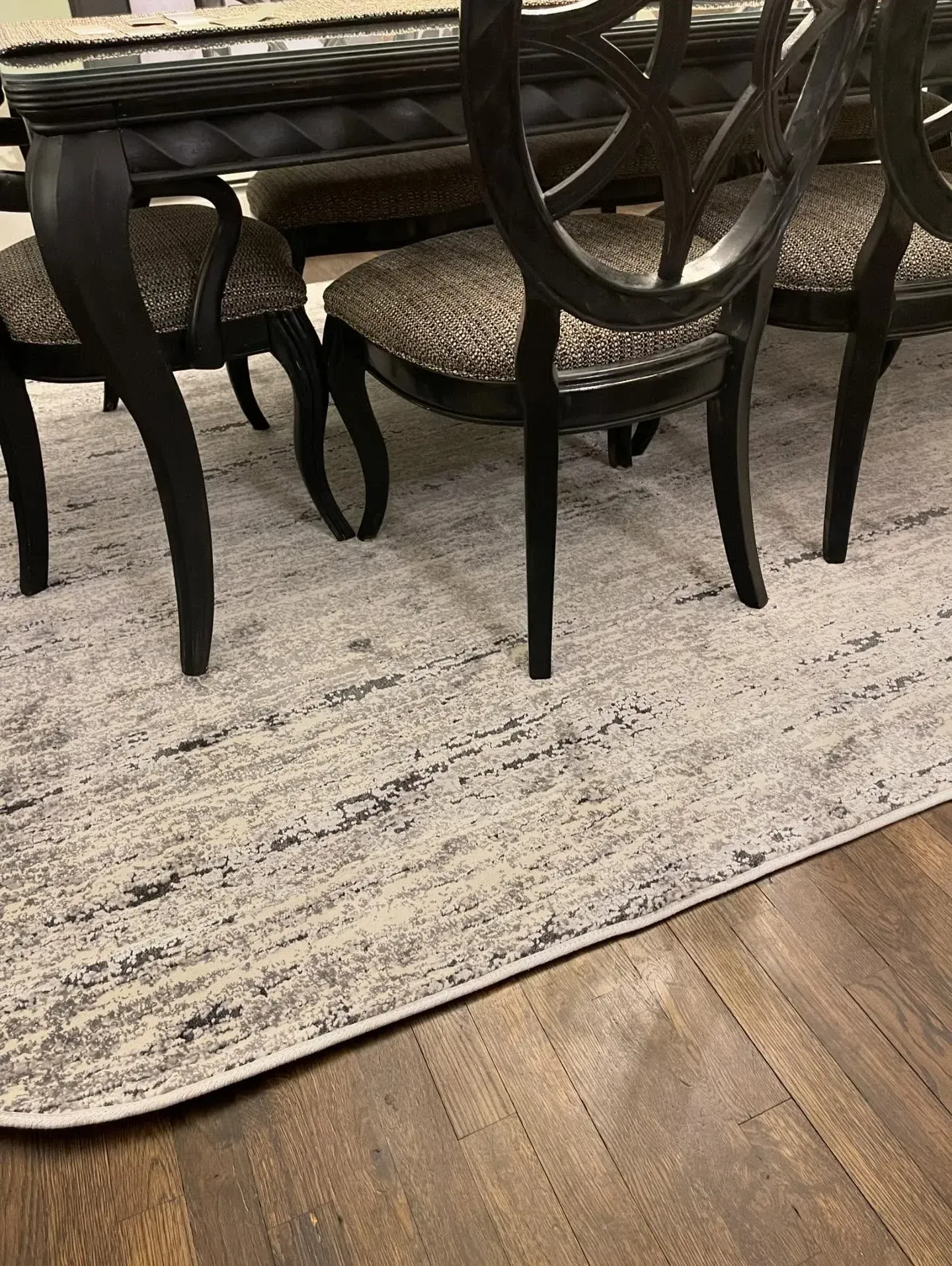 Wooden dining chairs around a table on a light patterned rug over hardwood flooring.
