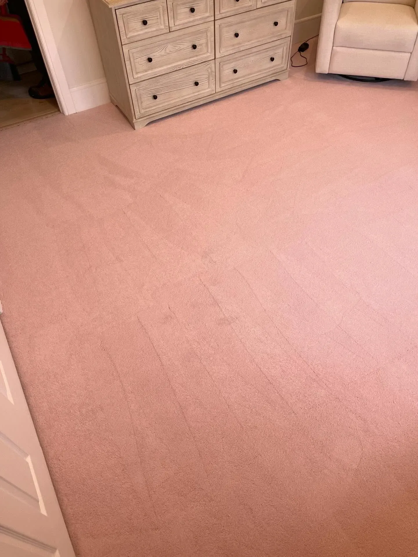 Pink carpeted bedroom floor with white dresser and chair in the corner