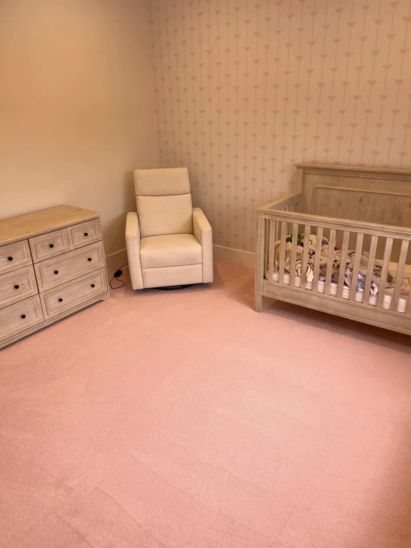 Pink nursery with crib, armchair, and dresser against wallpapered walls