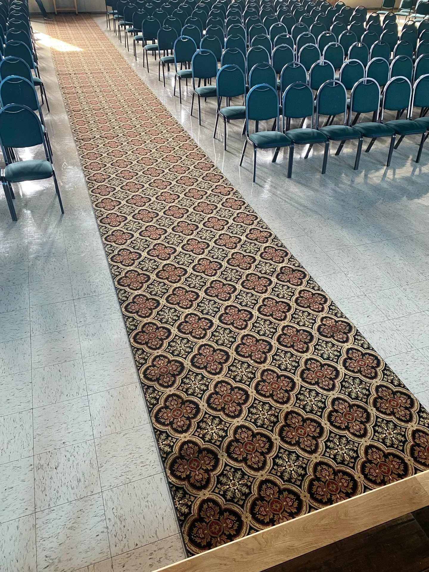 A carpeted aisle between rows of empty blue chairs in a hall.