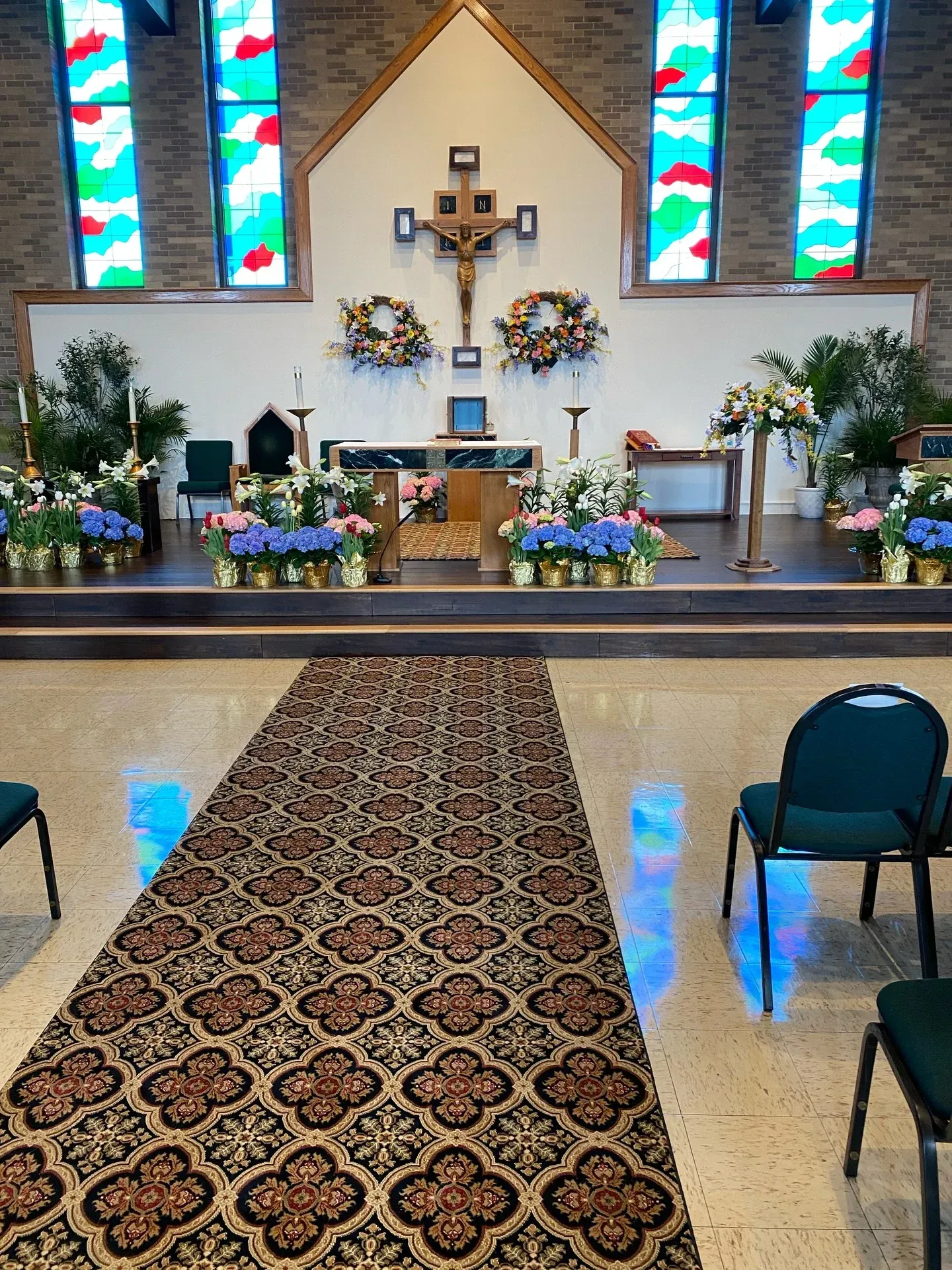 Church sanctuary with altar, cross, stained glass windows, and flower arrangements along the center aisle