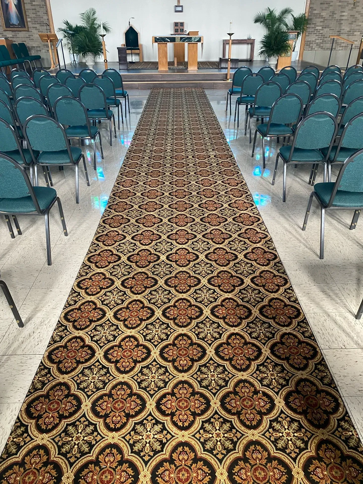Aisle in a chapel with teal chairs, patterned runner, and altar at the front.