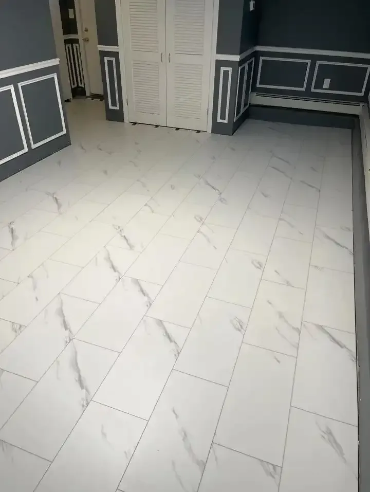 Empty room with white marble tile floor and dark paneled walls with white trim.