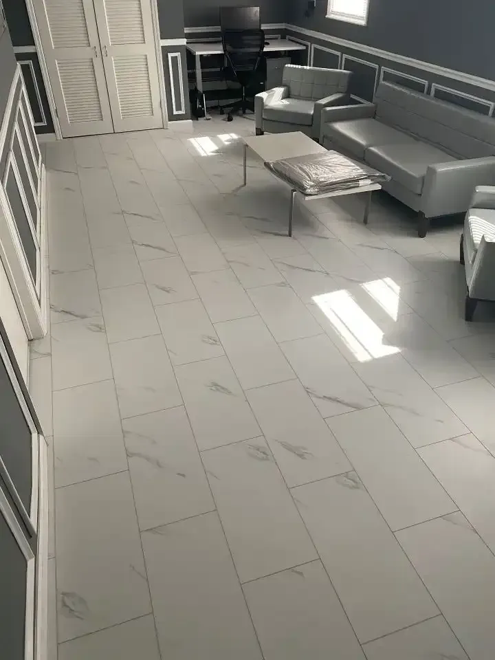 Modern living room with gray sofa, chaise lounge, desk, and tiled floor lit by sunlight