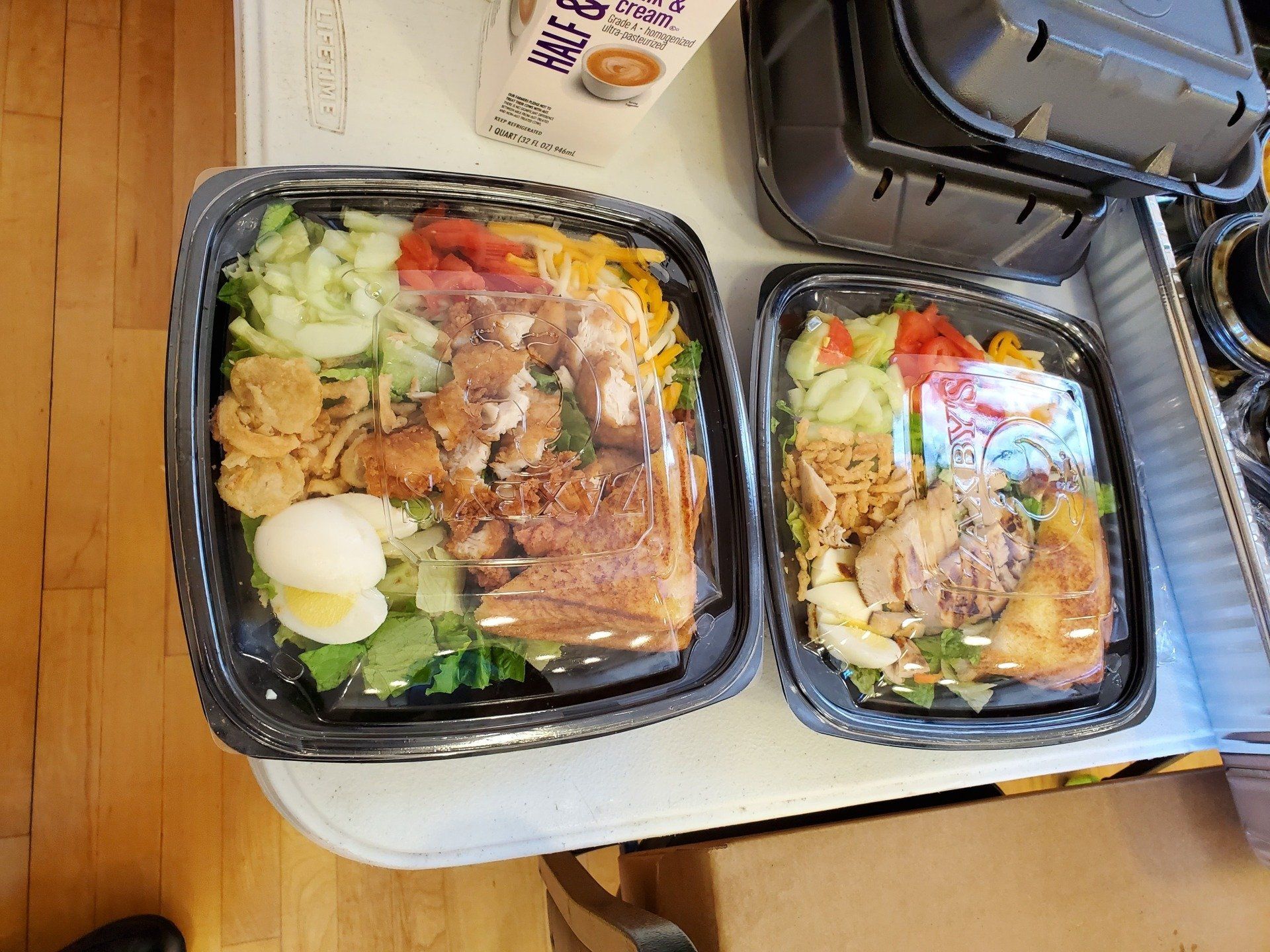 Two containers of food are sitting on a table next to a carton of milk.