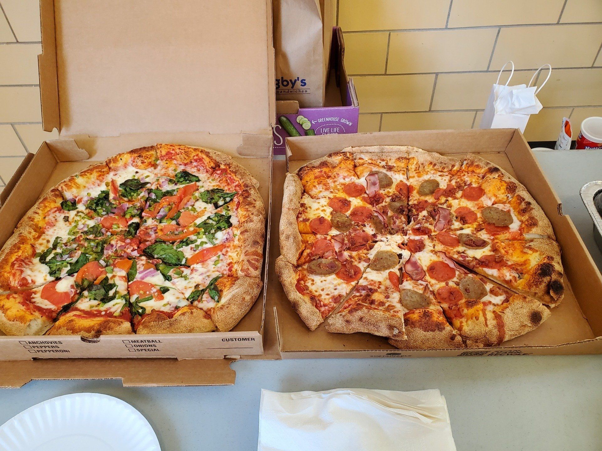 Two pizzas in cardboard boxes are sitting on a table.