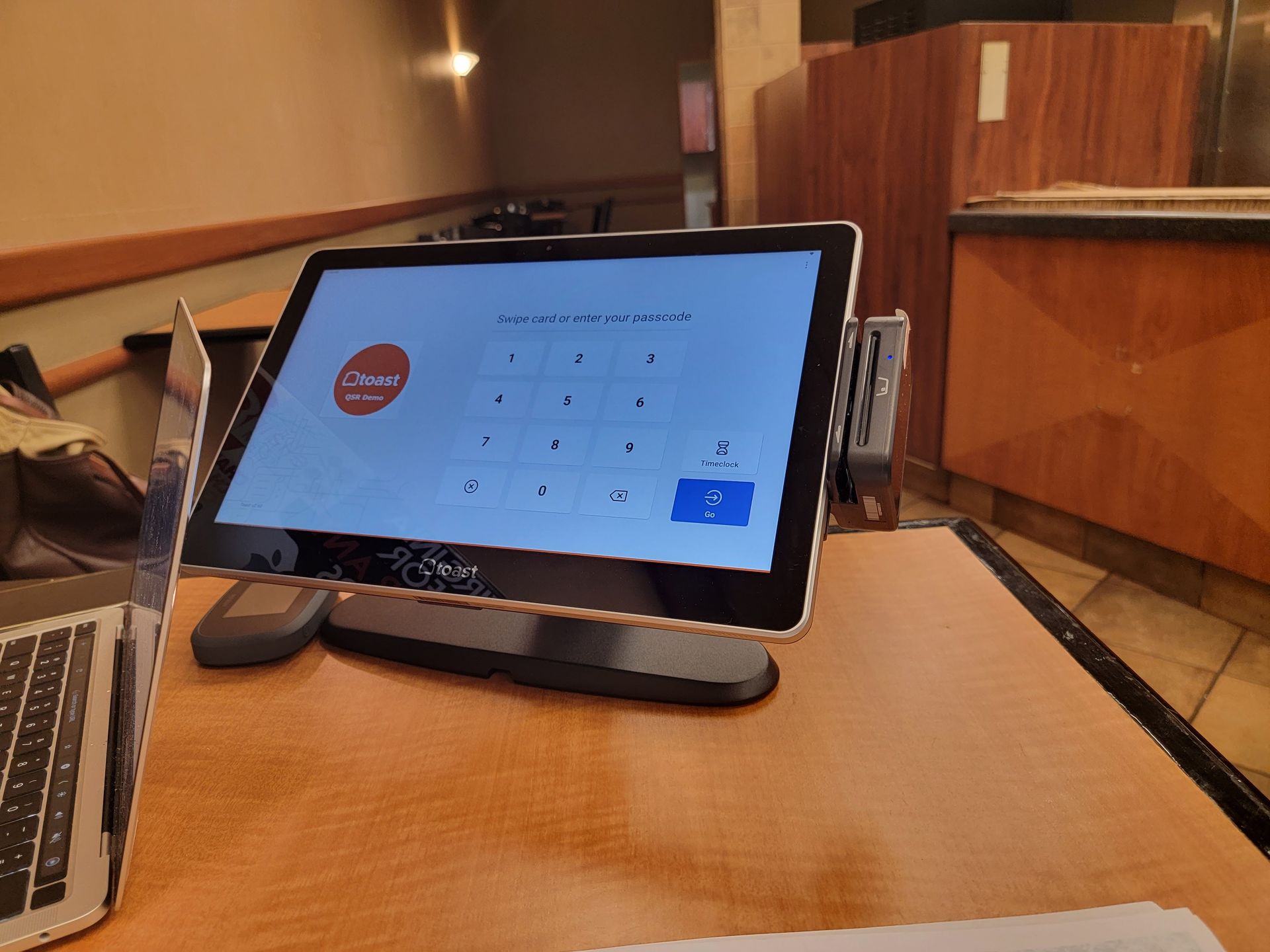 A tablet is sitting on a wooden table next to a laptop.