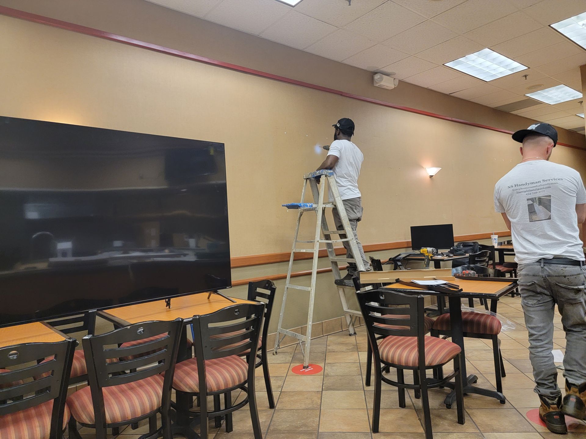 Two men are painting a wall in a restaurant.