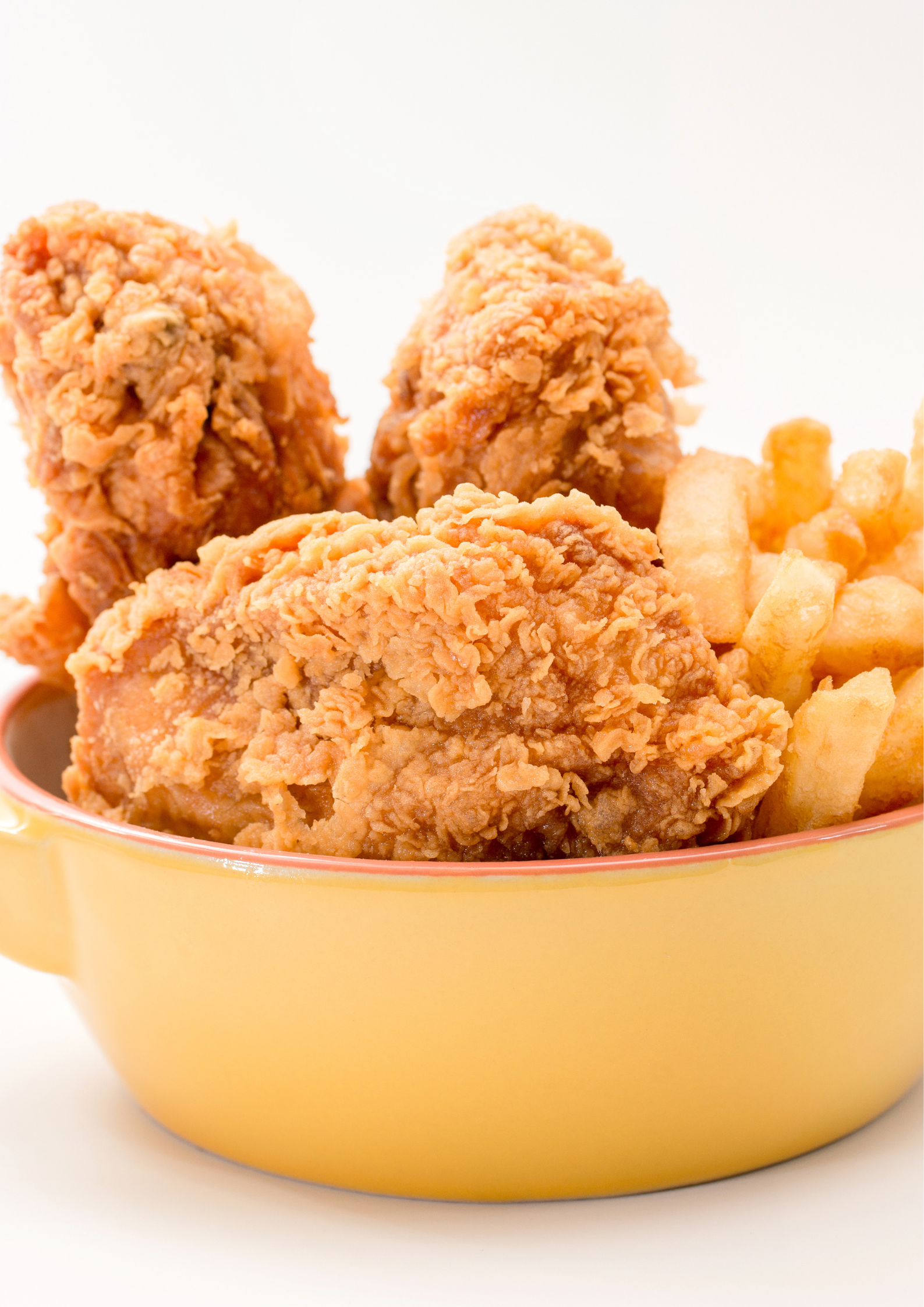 Fried chicken and french fries in a yellow bowl on a white background.
