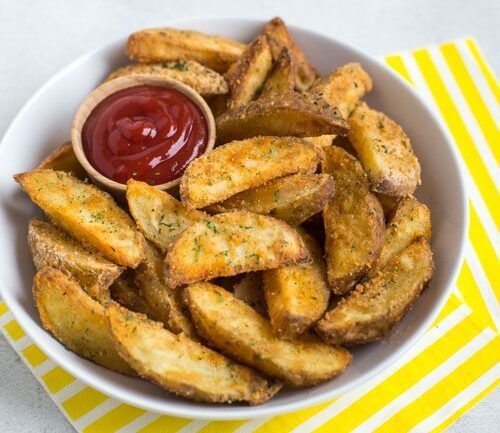 A bowl of potato wedges with ketchup on a yellow napkin.