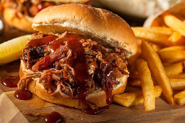 A pulled pork sandwich and french fries on a wooden cutting board.