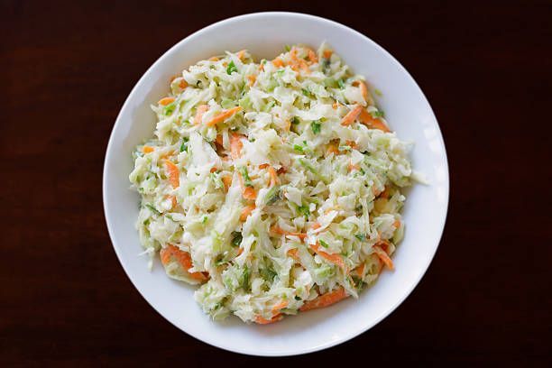 A white plate topped with coleslaw and carrots on a wooden table.