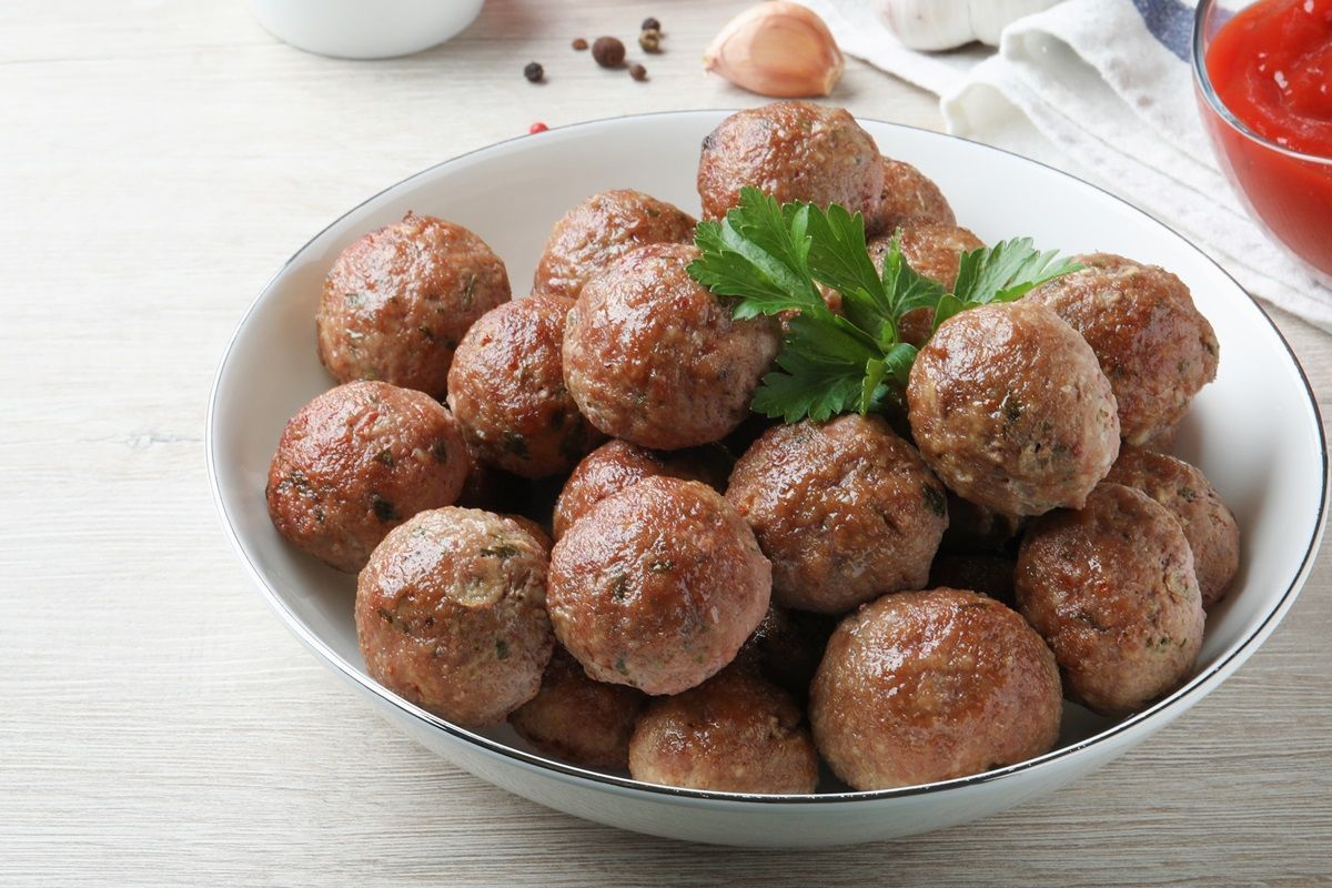 A white bowl filled with meatballs and parsley on a table.