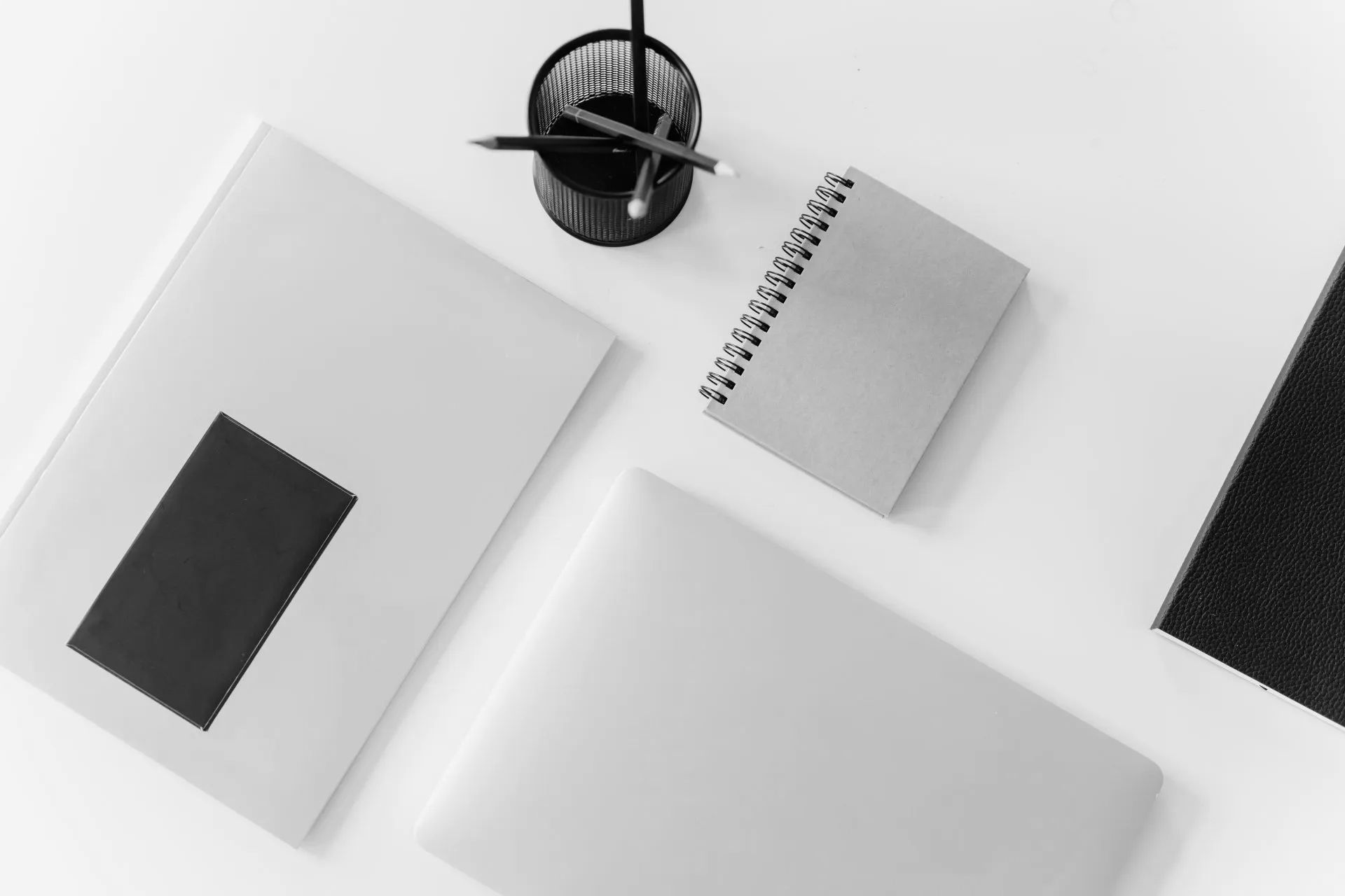 A desk with a laptop , notebooks , pencils , and a pen holder.