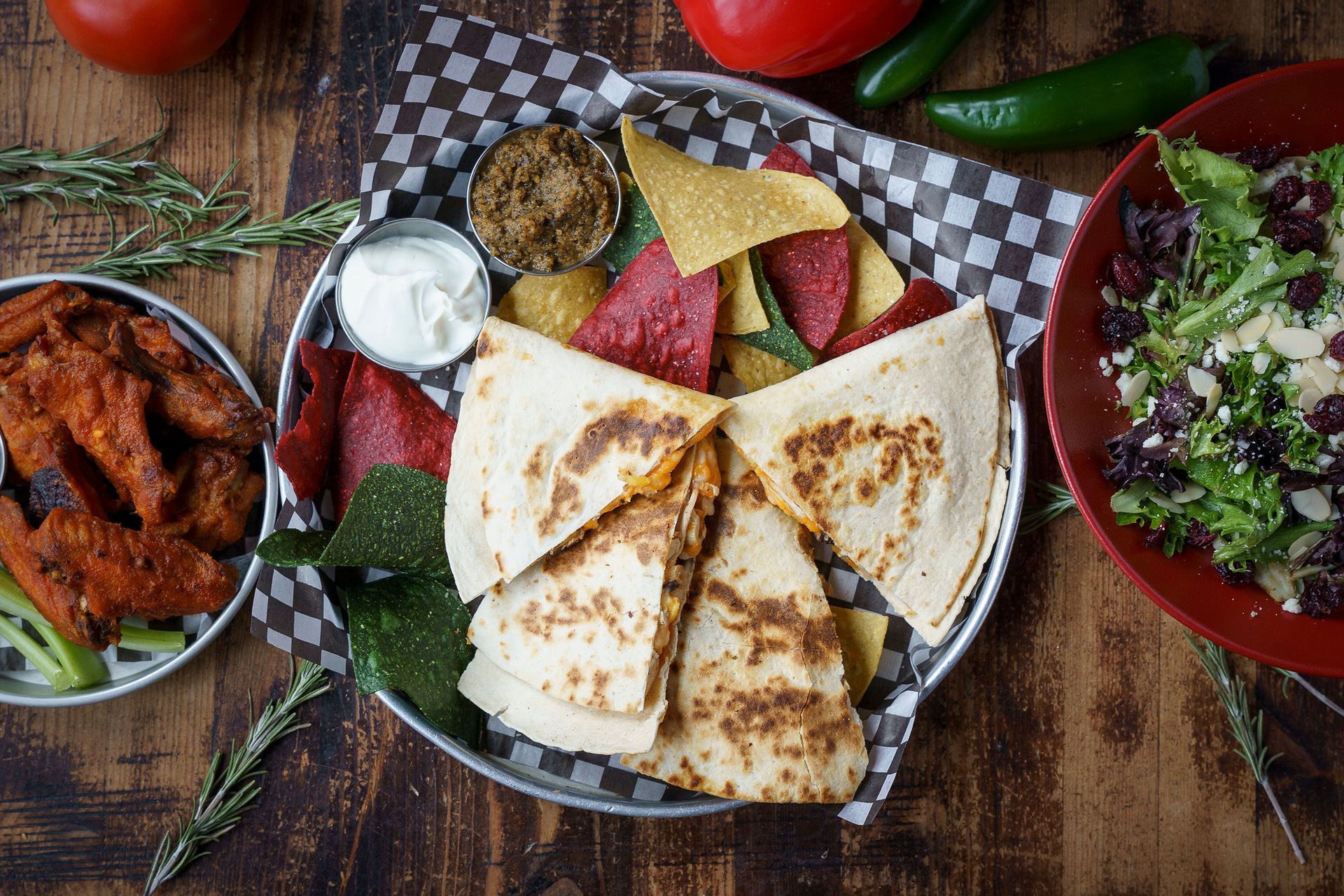 A spread of Mexican dishes: quesadillas, nachos, wings, salad, on a wood table.