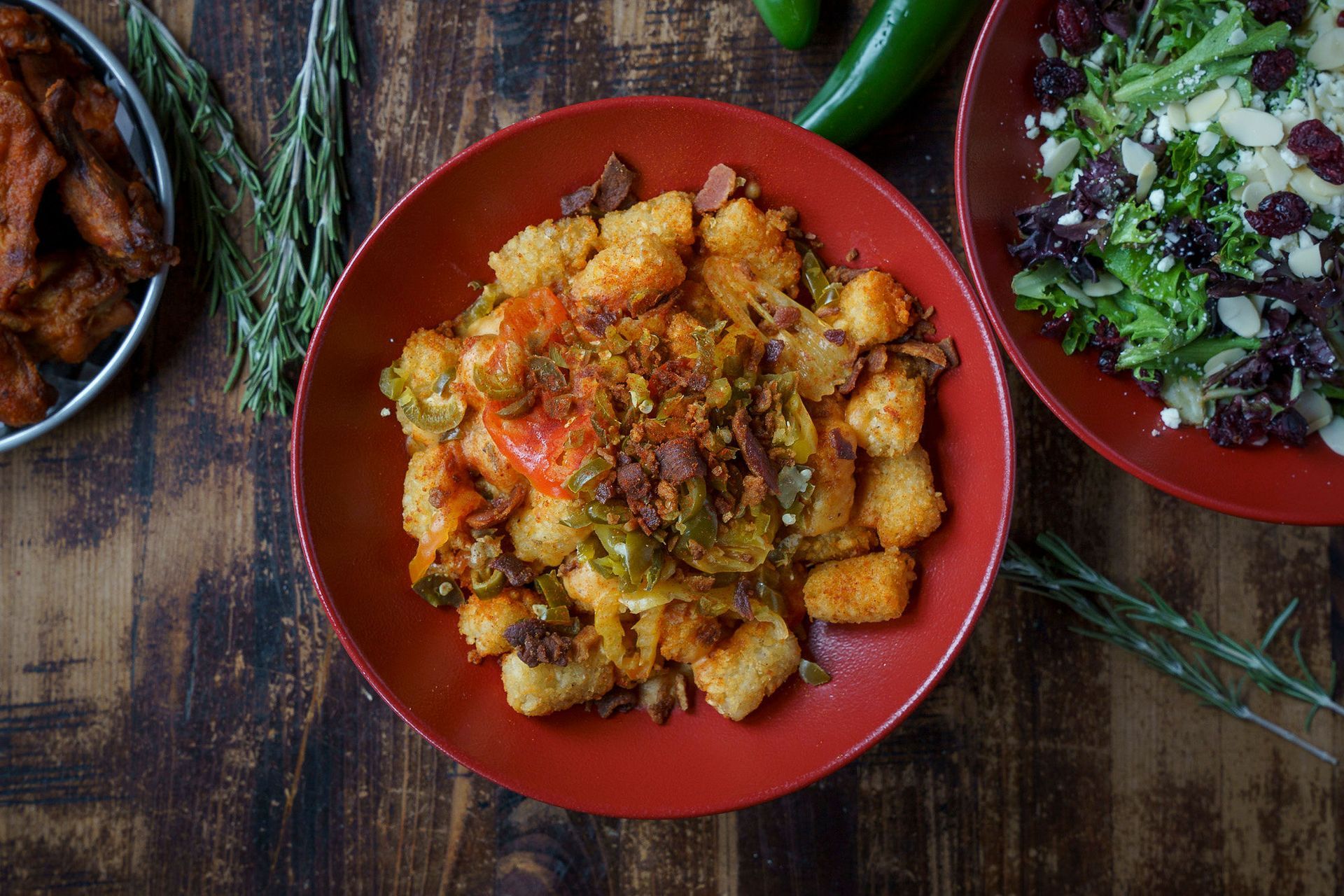 Tater tot bowl with bacon, peppers, and a side salad on a wooden table.