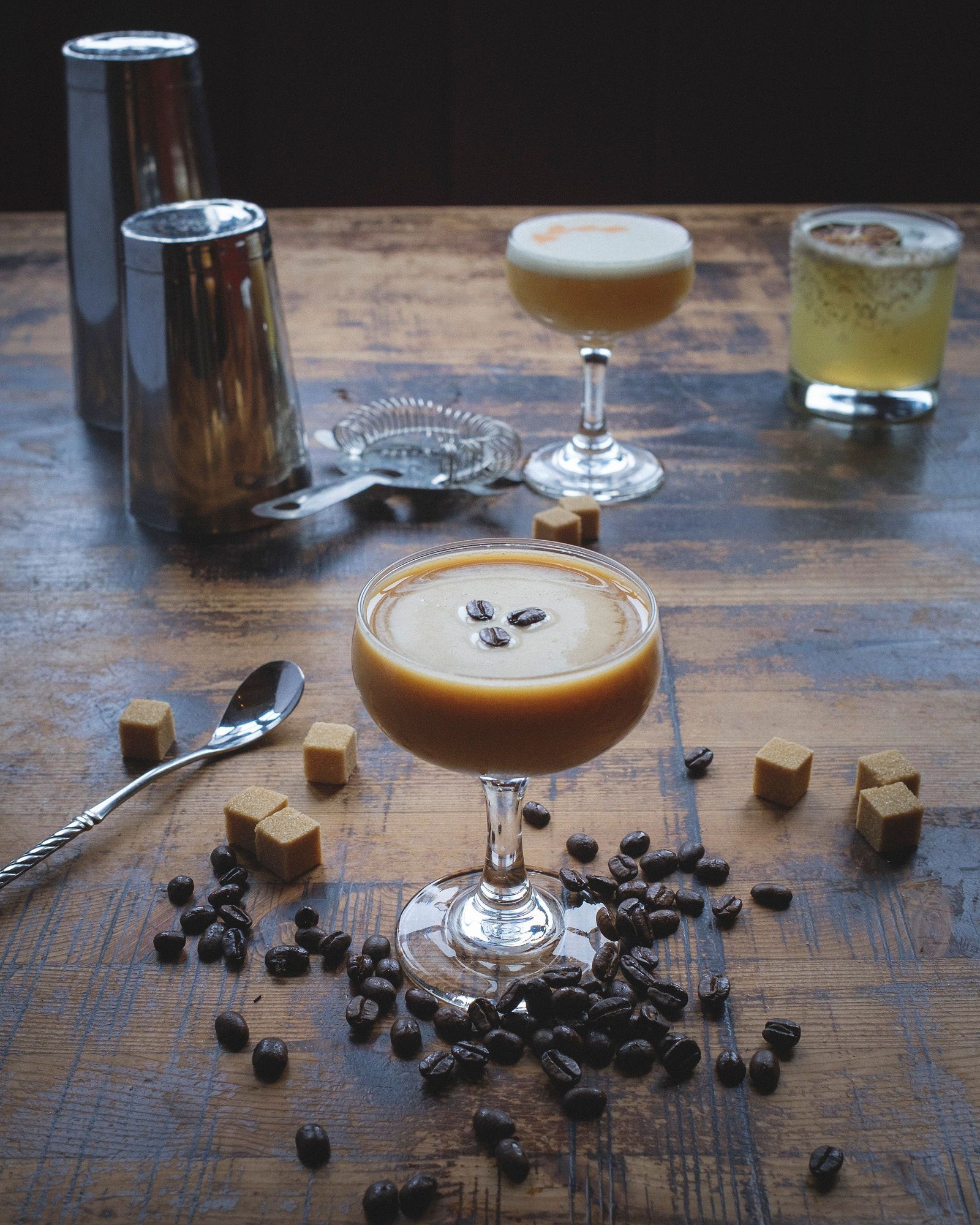 Espresso martini with coffee beans and caramels on a wood surface, with cocktail shaker.