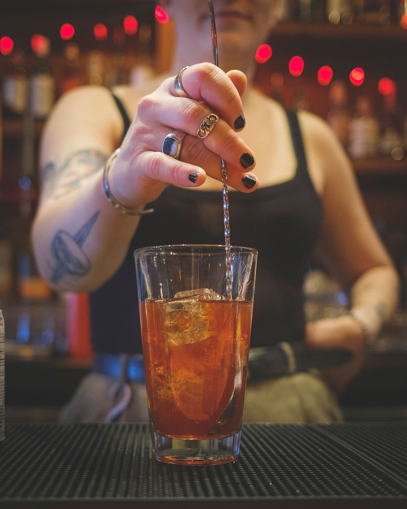 Bartender stirring a drink in a glass with ice. Dark bar setting.