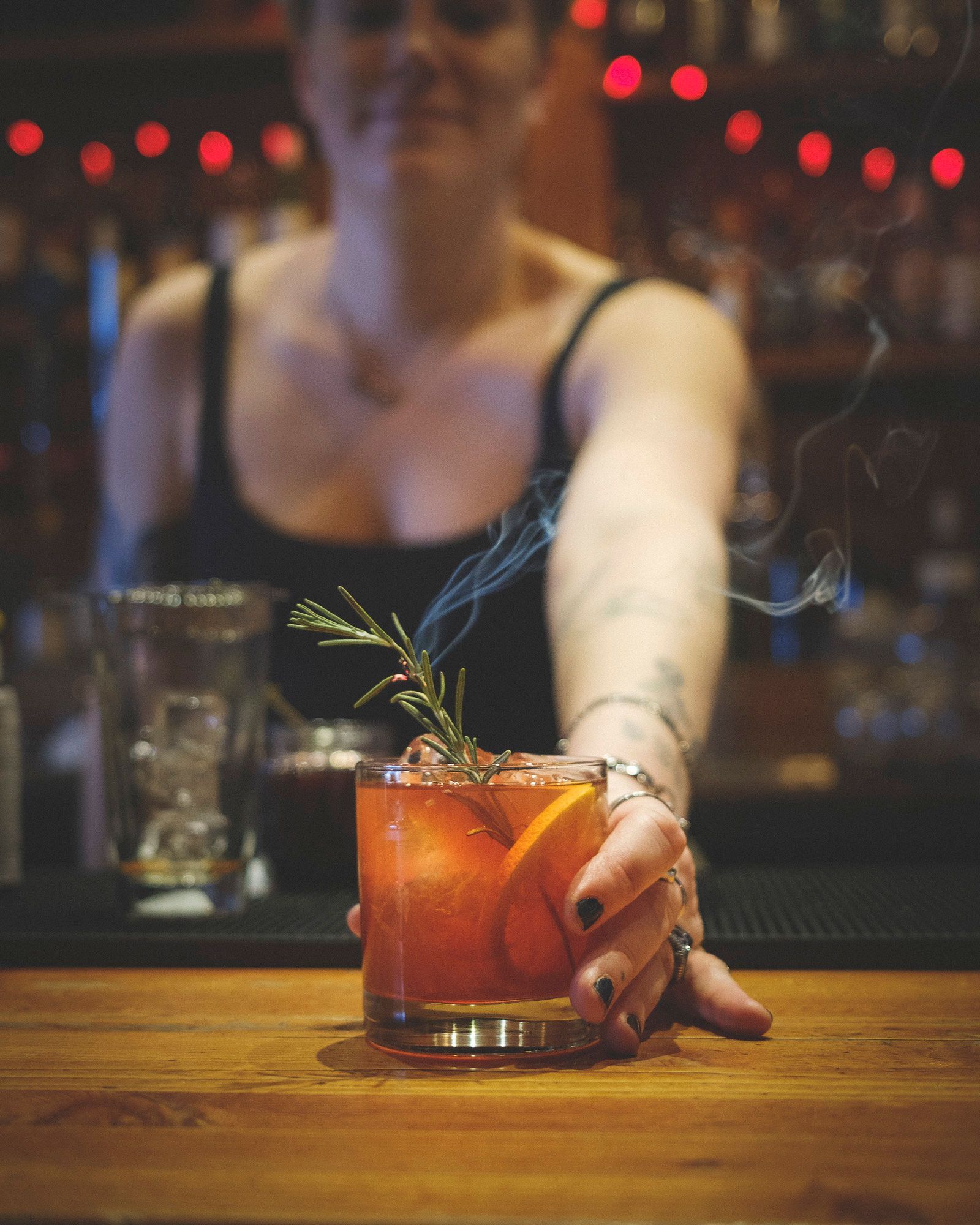 Devil's Elbow Bartender serving a smoky Negroni cocktail with an orange slice and rosemary garnish.