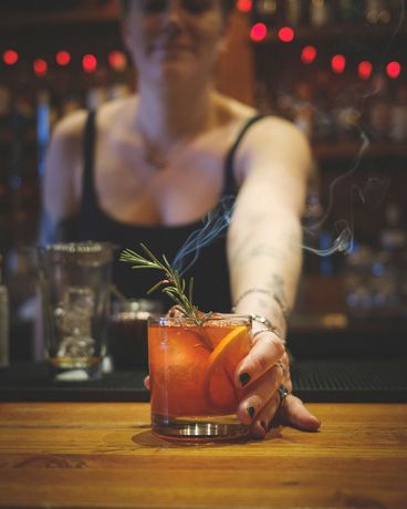 Devil's Elbow Bartender serving a smoky Negroni cocktail with an orange slice and rosemary garnish.