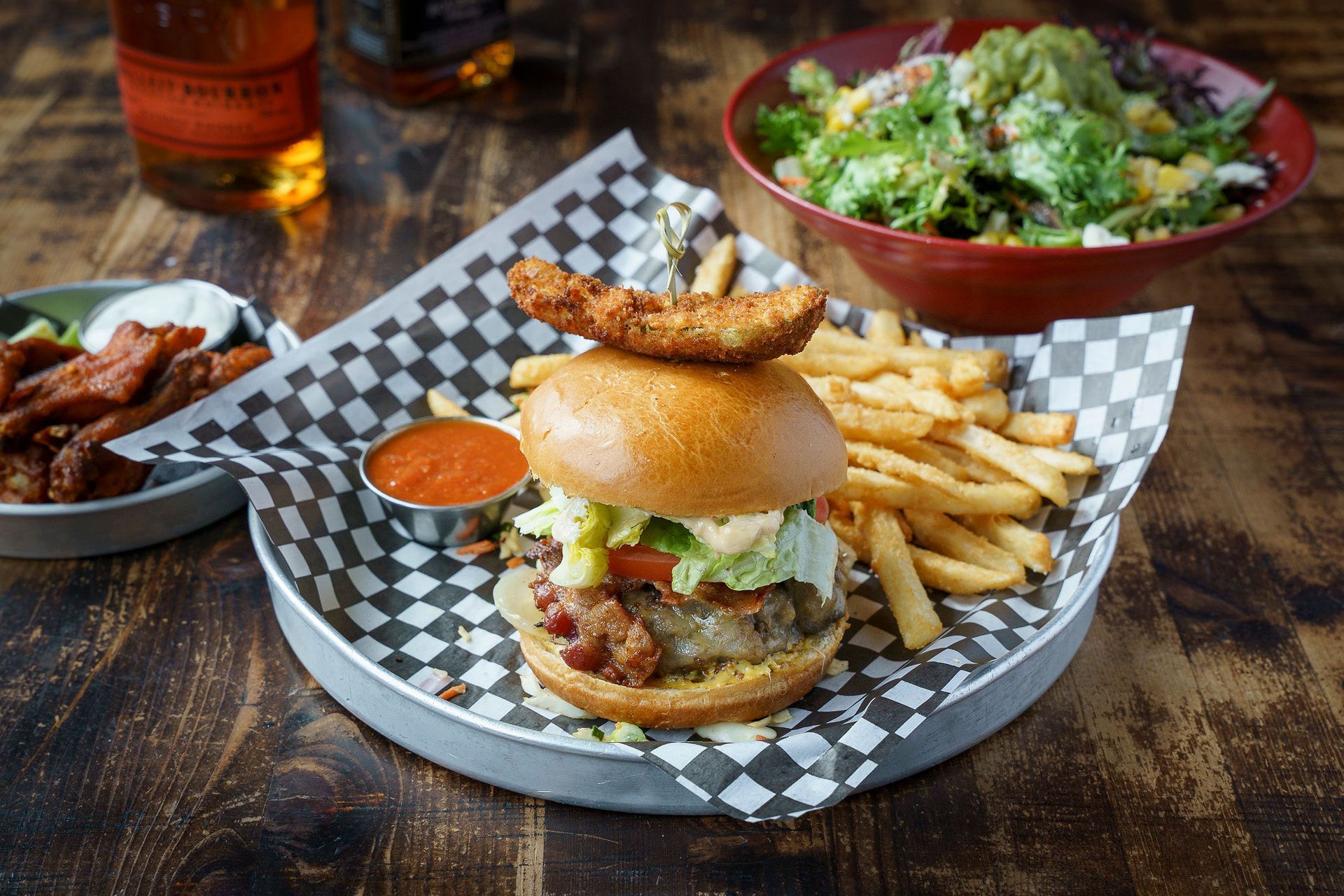 Burger with fries and a salad on a checkered plate, on a wooden table.