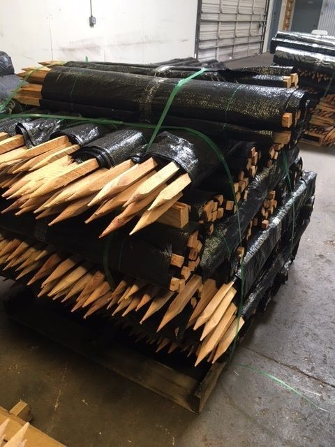 Bundles of sharpened wooden stakes tied with black plastic, stacked on a pallet in a warehouse.