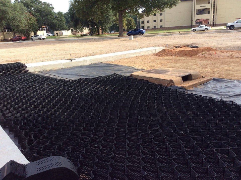 Black erosion control matting laid on bare ground at a construction site with trees and buildings nearby