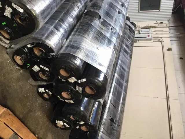 Stacks of black industrial cylinders wrapped in clear plastic on a warehouse floor